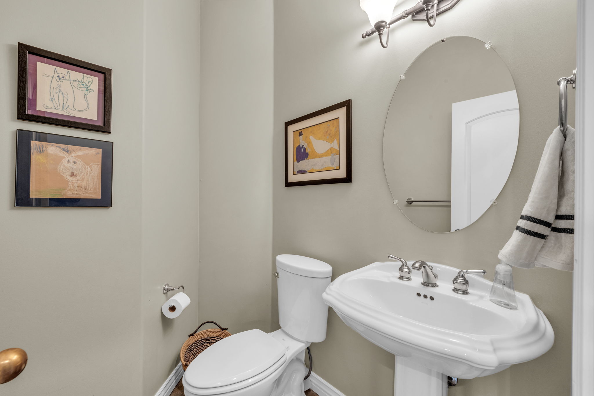 Pedestal sink with brushed nickel faucet, wall-mounted oval mirror, and overhead vanity lighting