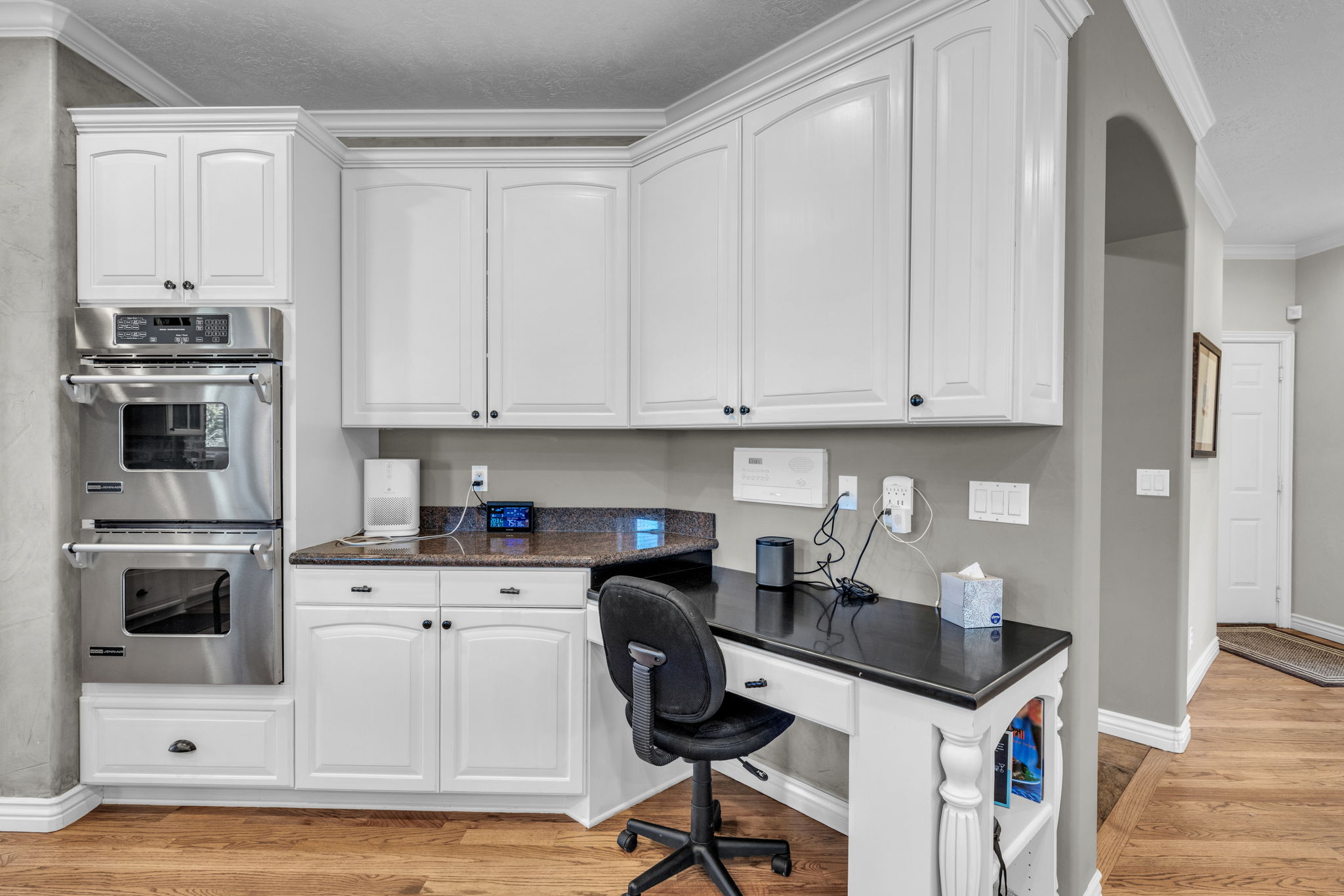 Custom built-in desk with black countertop, white cabinetry, and a double wall oven