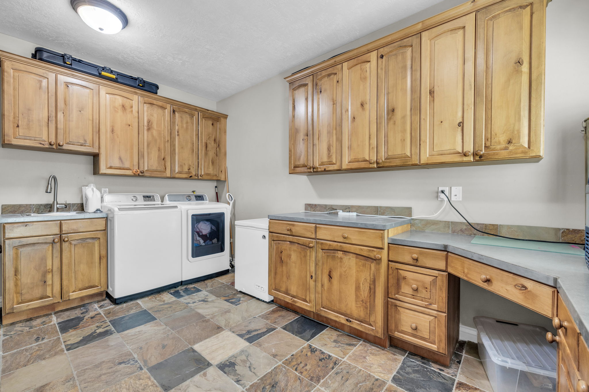 Utility room featuring extensive wood cabinetry, a built-in sink with a gooseneck faucet, durable stone-look tile flooring, and ample countertop space