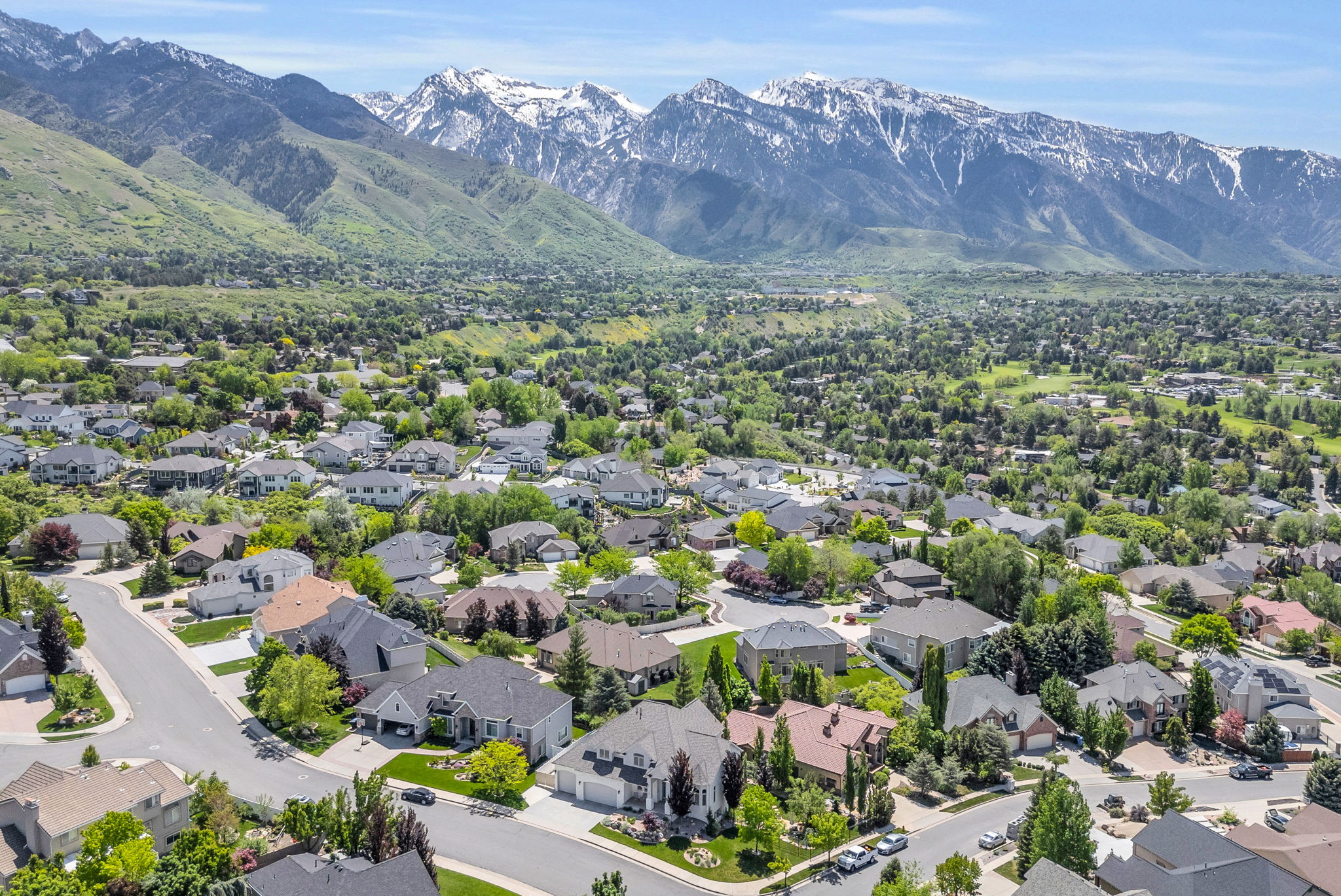 Aerial perspective showcasing a residential community with mature landscaping, framed by snow-capped mountains and verdant foothills