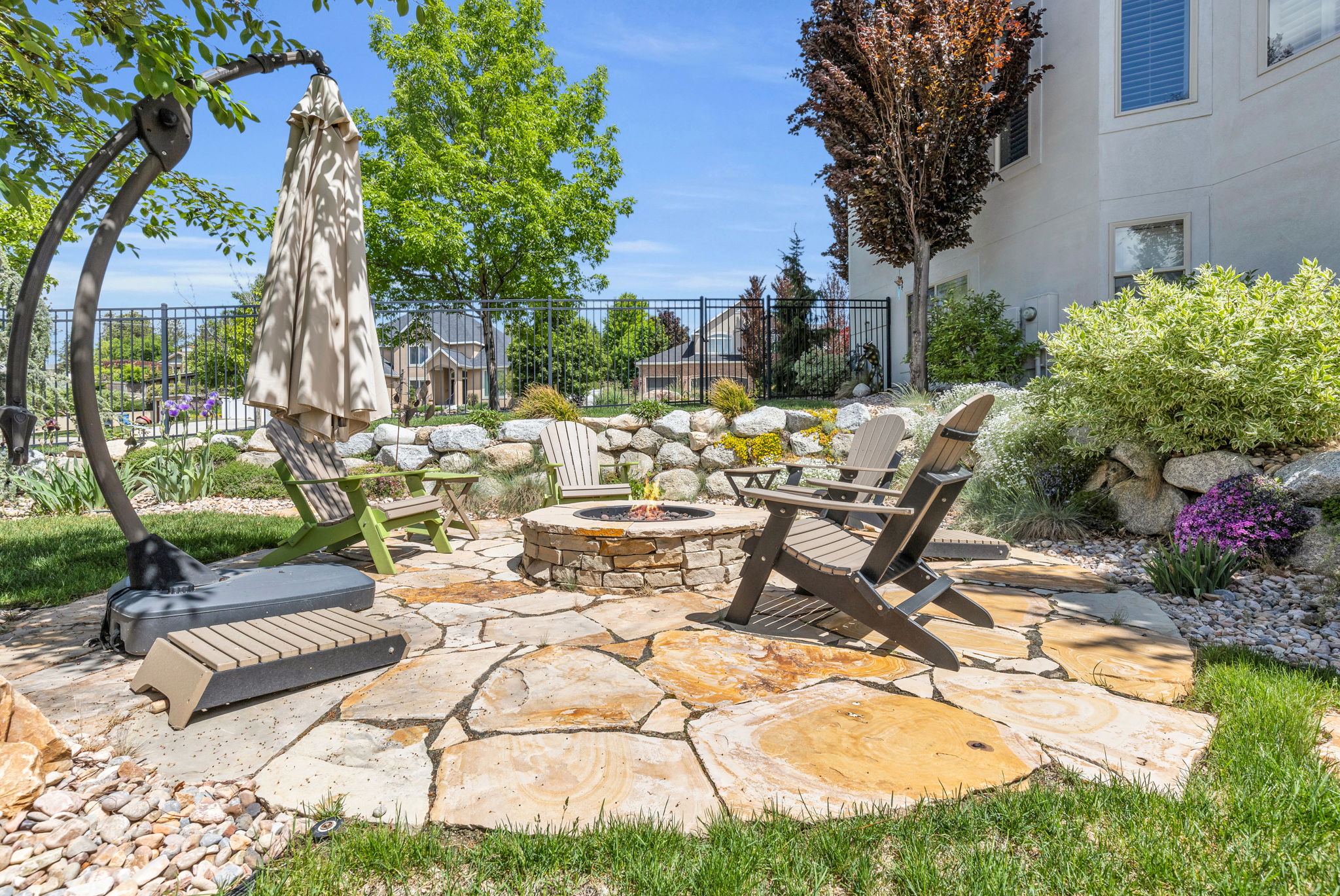 Flagstone patio featuring a stone-clad fire pit, surrounded by lush landscaping with mature trees and a rock-stacked retaining wall