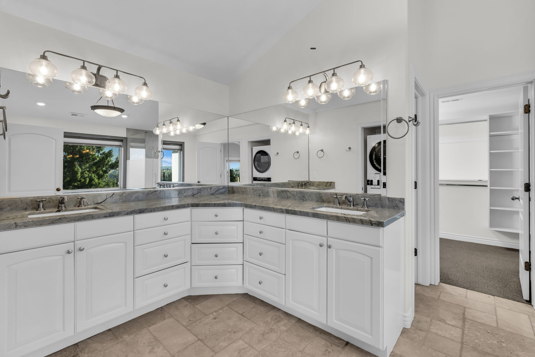 Expansive vanity featuring dual sinks, gray stone countertops, and extensive white cabinetry