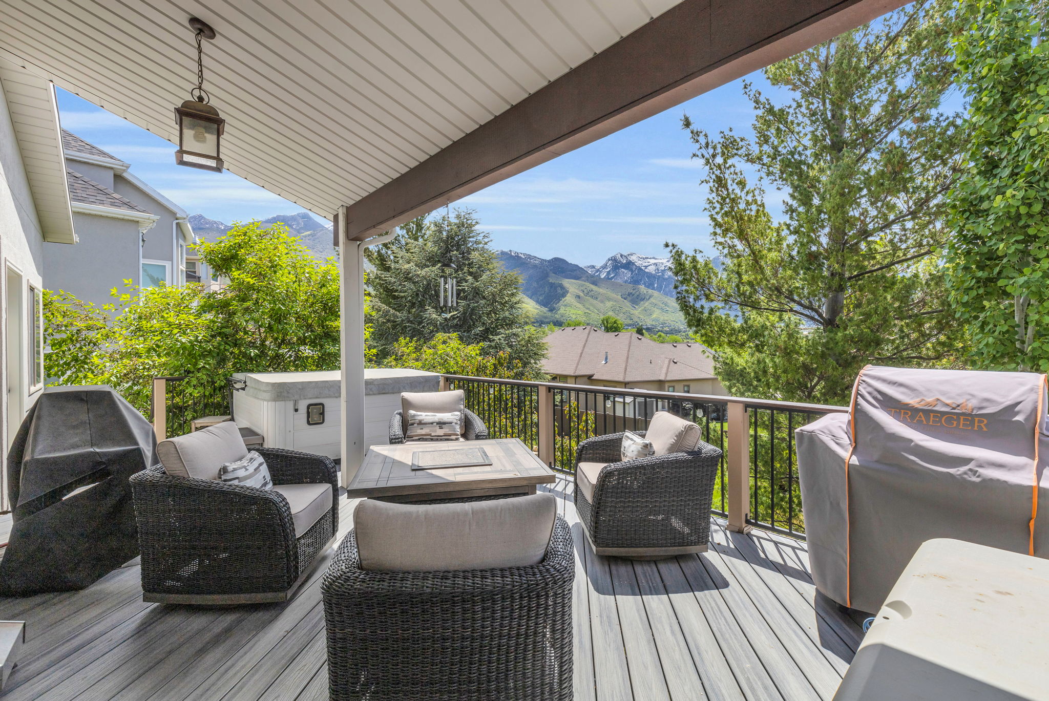 Covered outdoor deck featuring composite decking, a hot tub, and wood-finish railing with black balusters