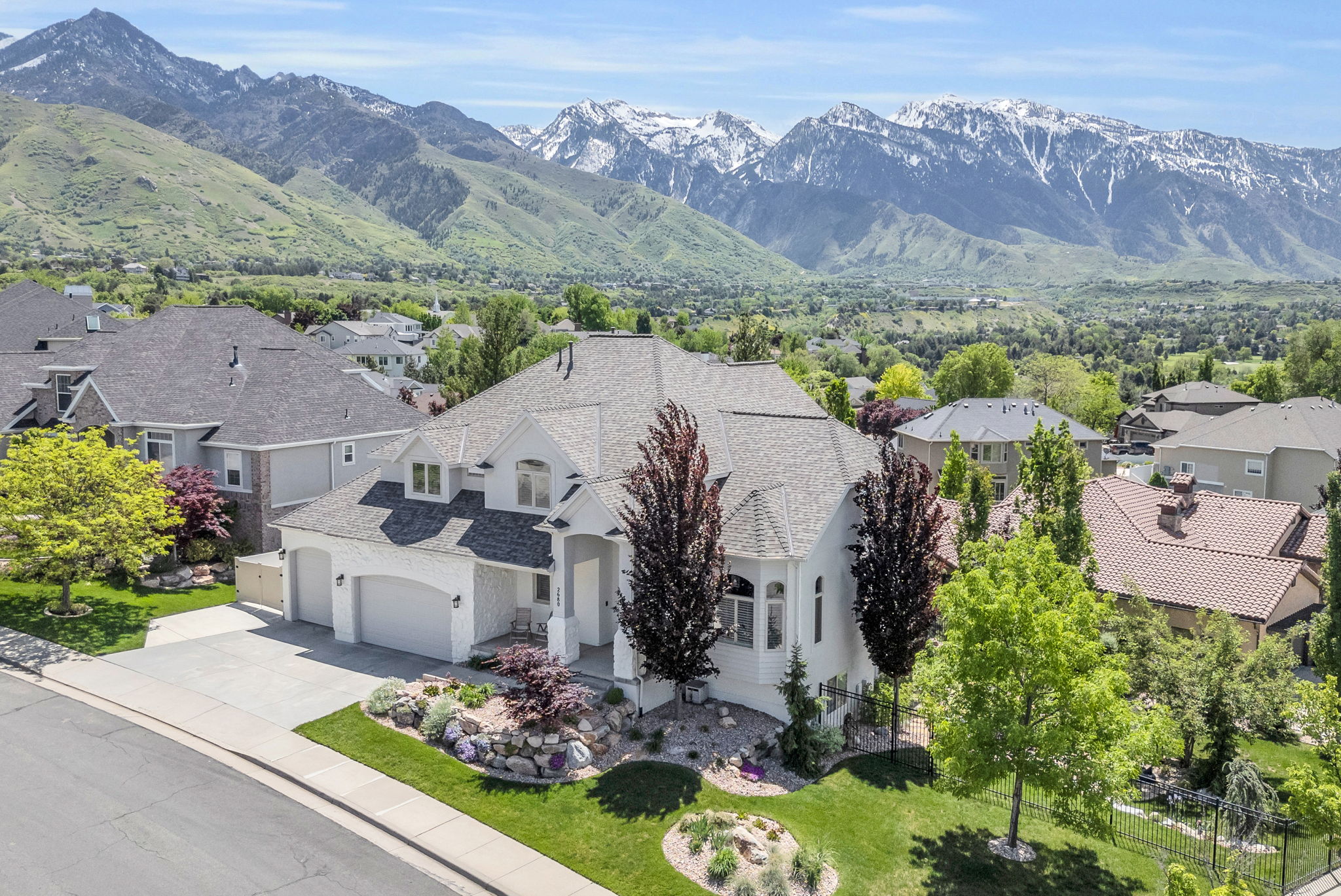 Stucco exterior residence with a multi-car garage, pitched shingle roof, and mature landscaping