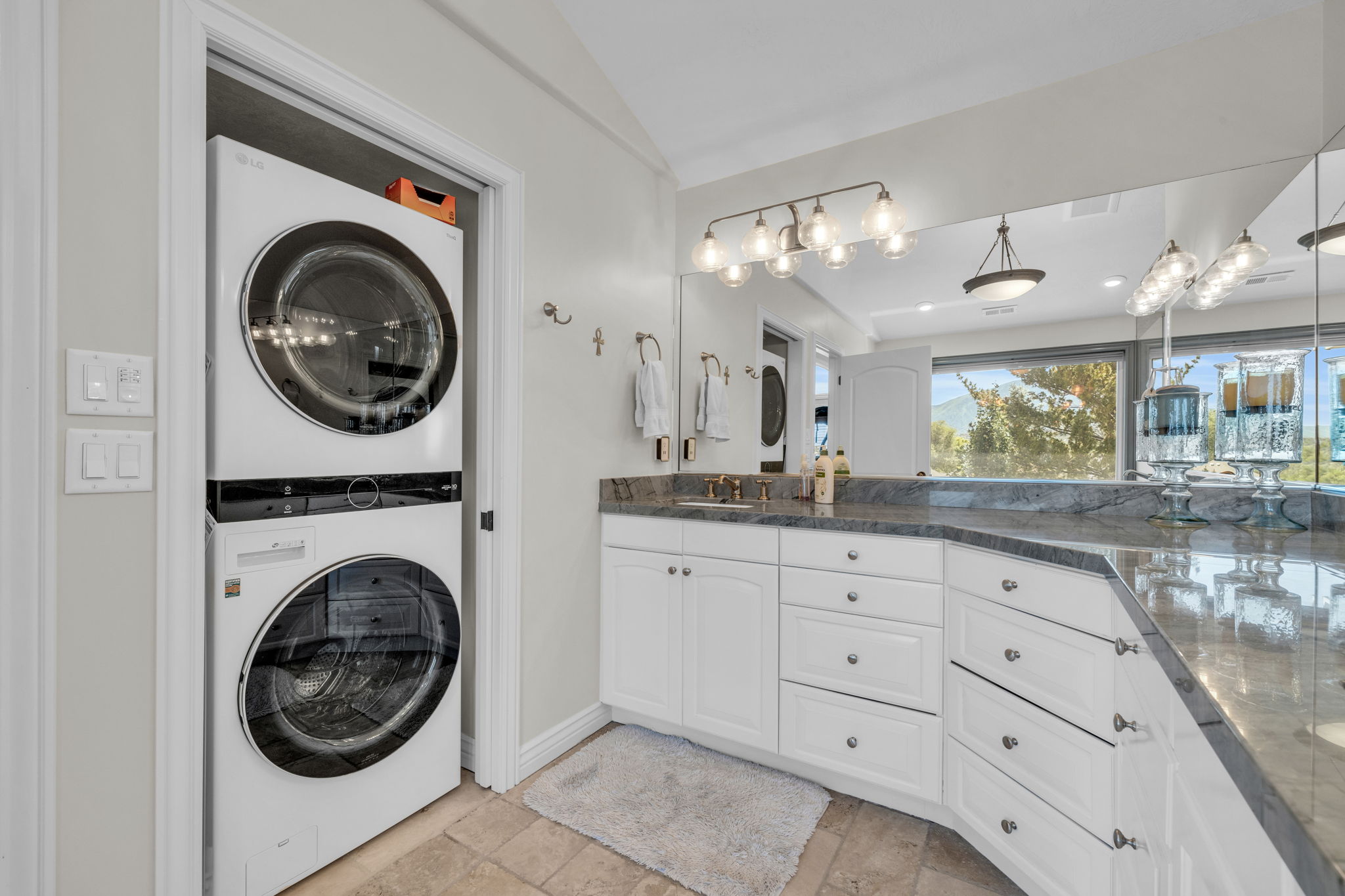 Integrated laundry stack featuring front-loading washer and dryer, complemented by a vanity with white cabinetry, a stone countertop, and an expansive mirror