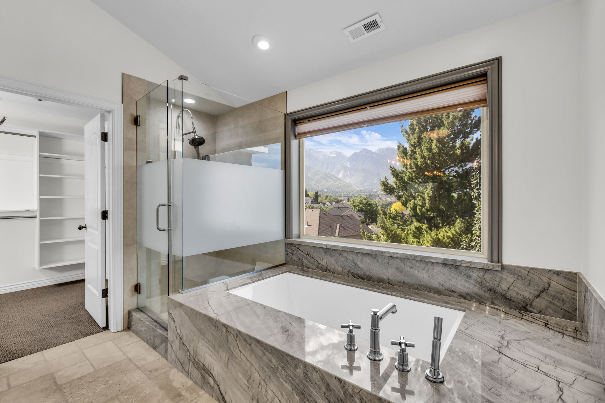 Bathroom featuring a built-in soaking tub with a stone surround, a walk-in shower with a glass enclosure, and a large window showcasing a mountain backdrop