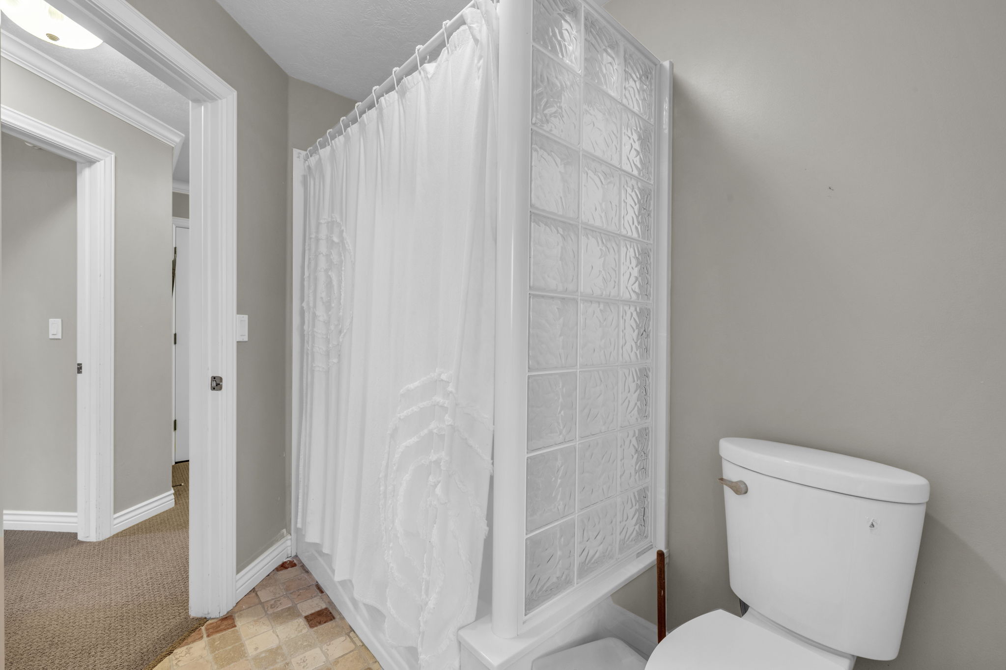 Bathroom featuring a glass block shower enclosure, white porcelain toilet, and neutral wall paint
