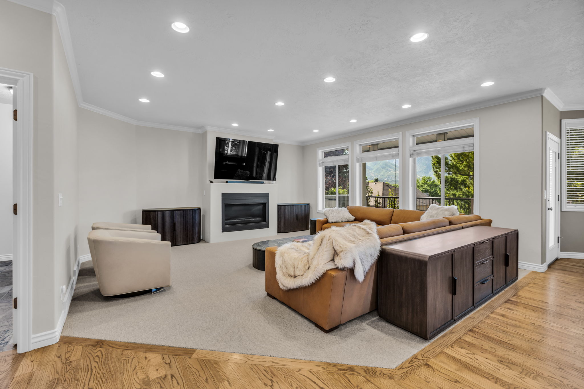 Spacious living area featuring a fireplace, multiple recessed lights, abundant natural light from numerous windows, crown molding, and wood-finish flooring