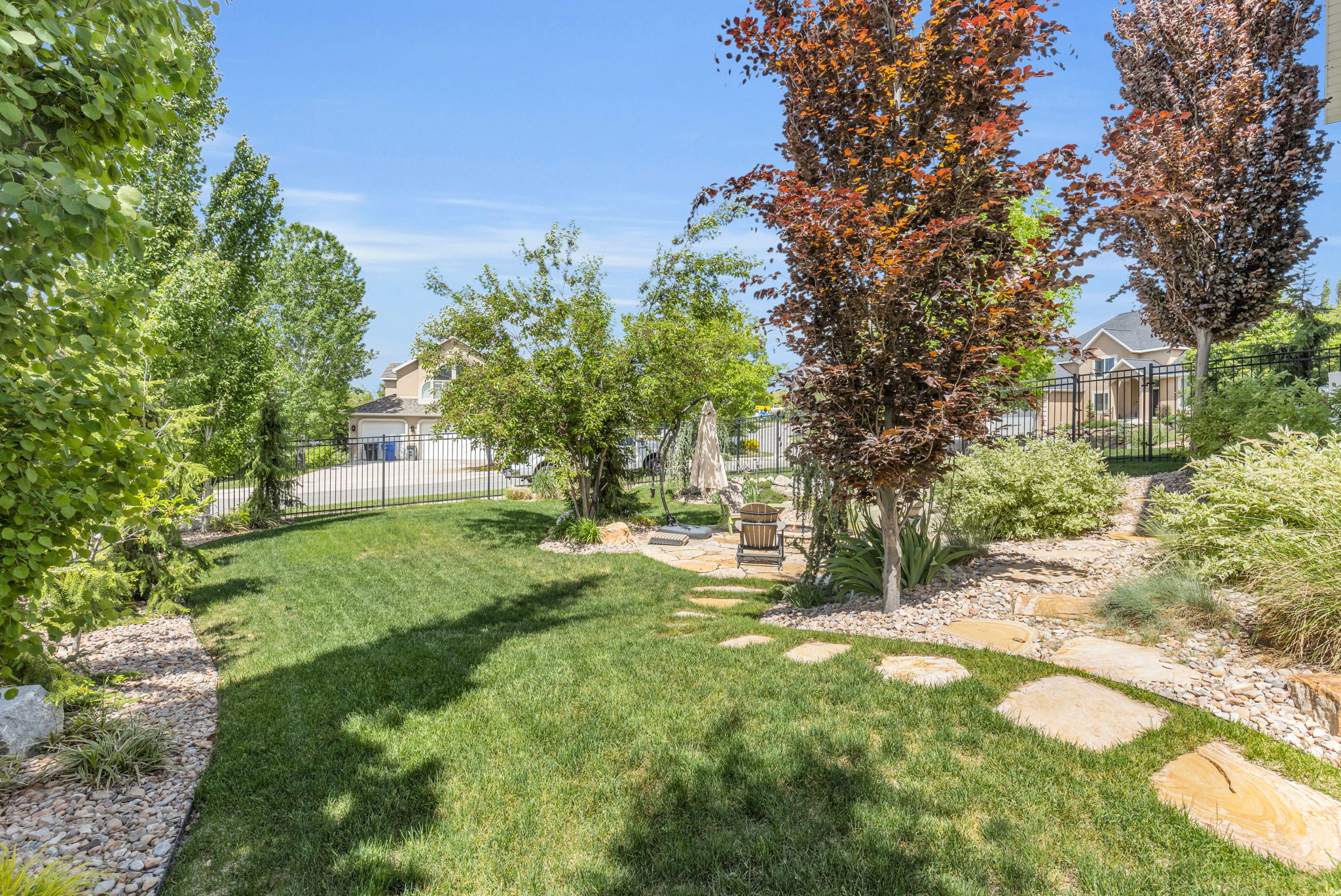 Expansive backyard featuring a manicured lawn, established landscaping, and a flagstone pathway leading to a patio area