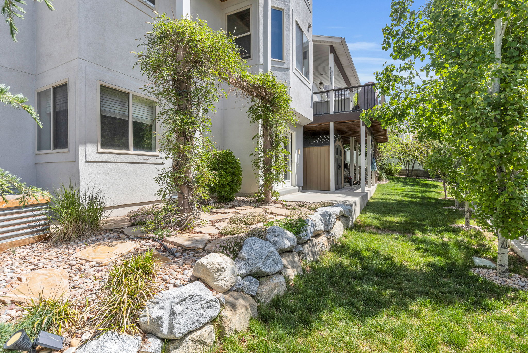 Exterior stucco finish with a ground-level patio, natural stone retaining wall, and verdant lawn