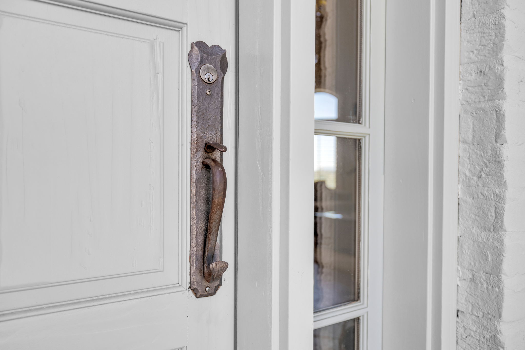 White entry door with a dark-toned ornate handle set, flanked by a sidelight with divided lites, and an exterior white-painted brick facade