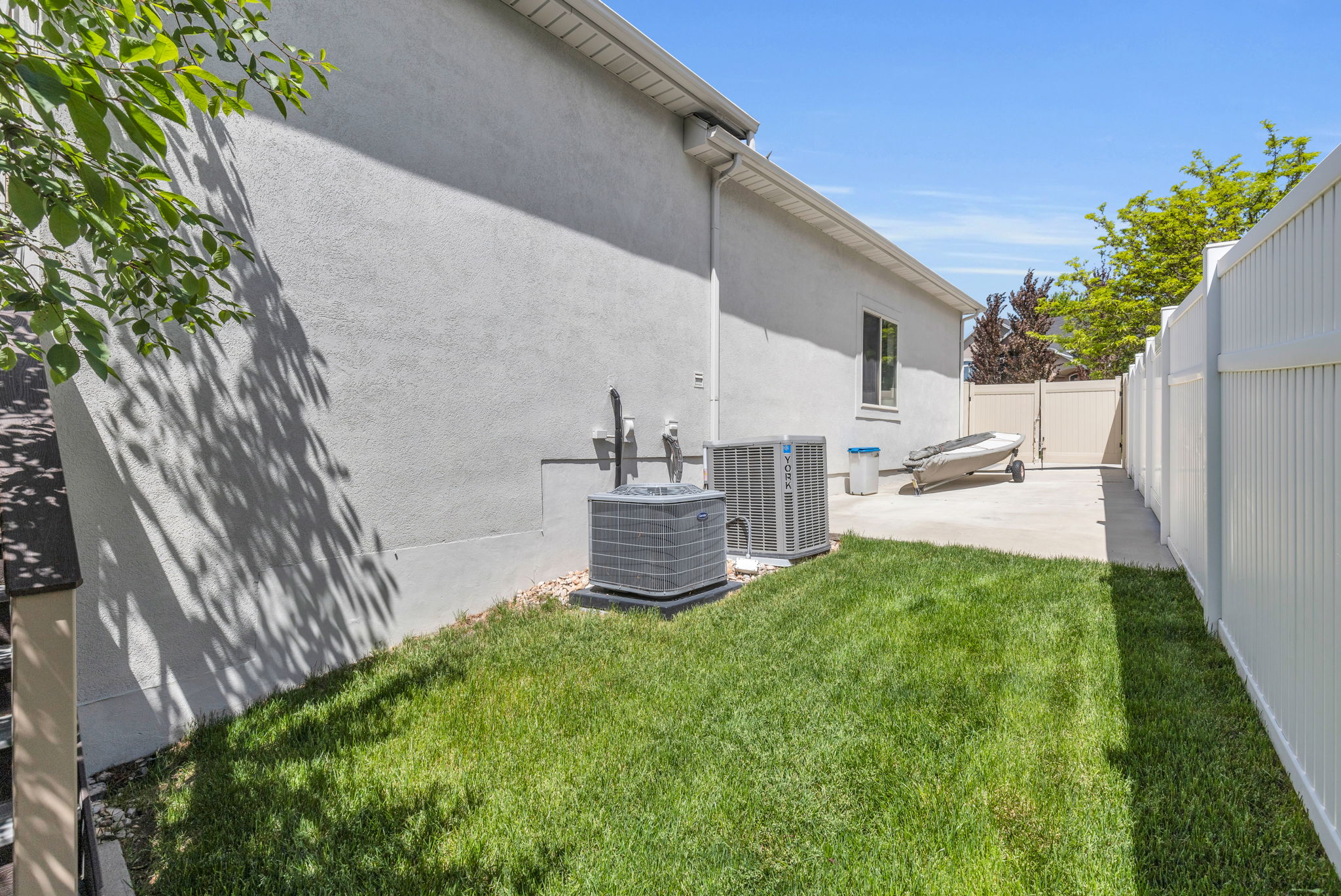 Manicured side yard featuring a lush lawn, white vinyl privacy fencing, and a concrete patio area with a tan double gate