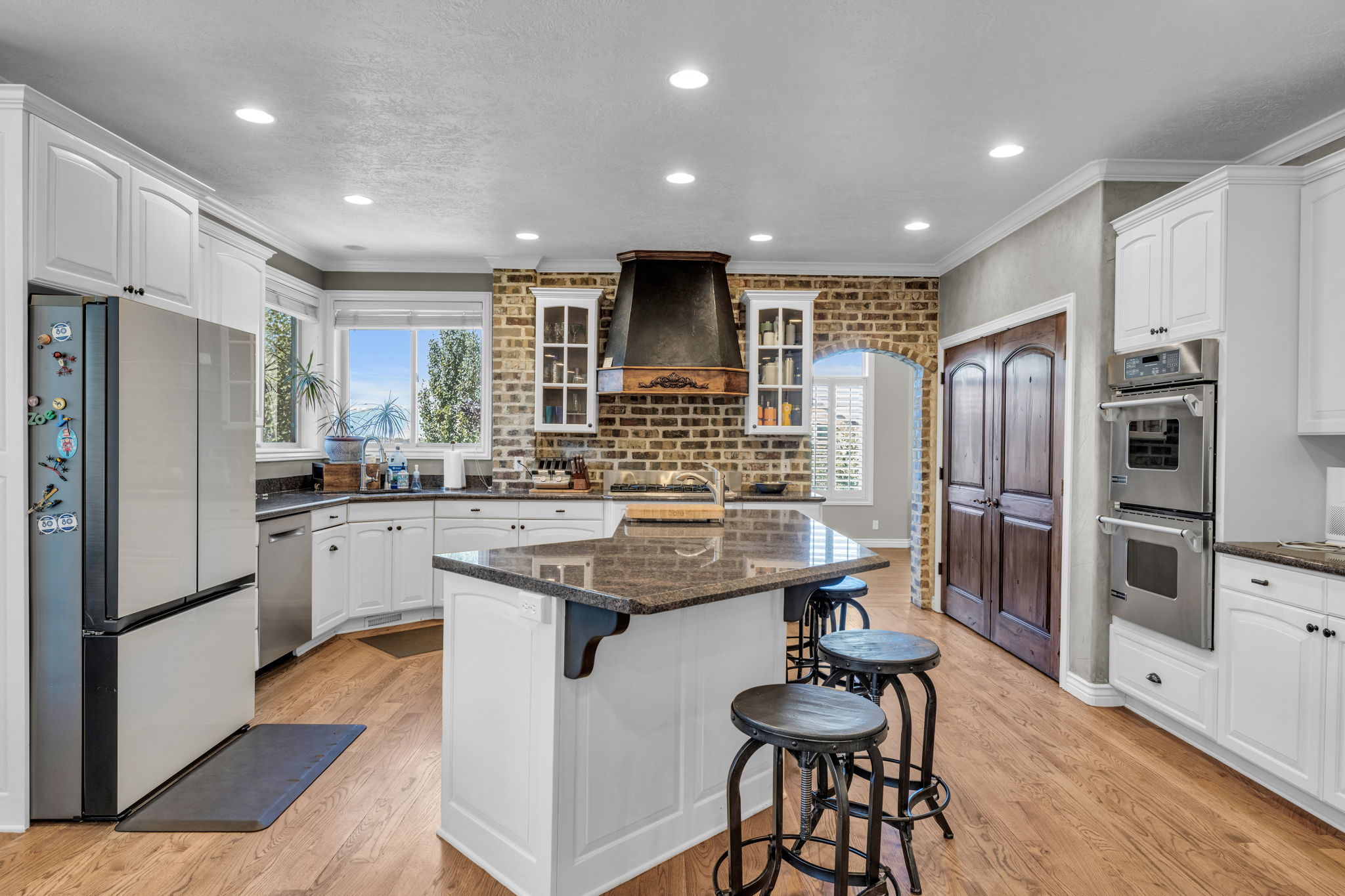 Gourmet kitchen featuring a central island with a stone countertop, white cabinetry, stainless steel appliances, brick-finish backsplash, and wood-finish flooring
