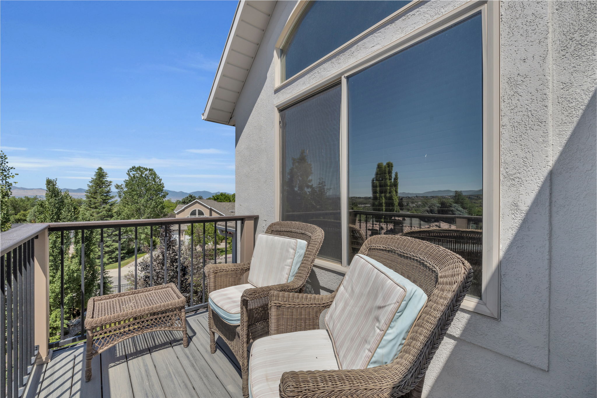 Private balcony off of primary, featuring composite decking, metal railings, and an expansive outdoor backdrop of distant hills and mature trees