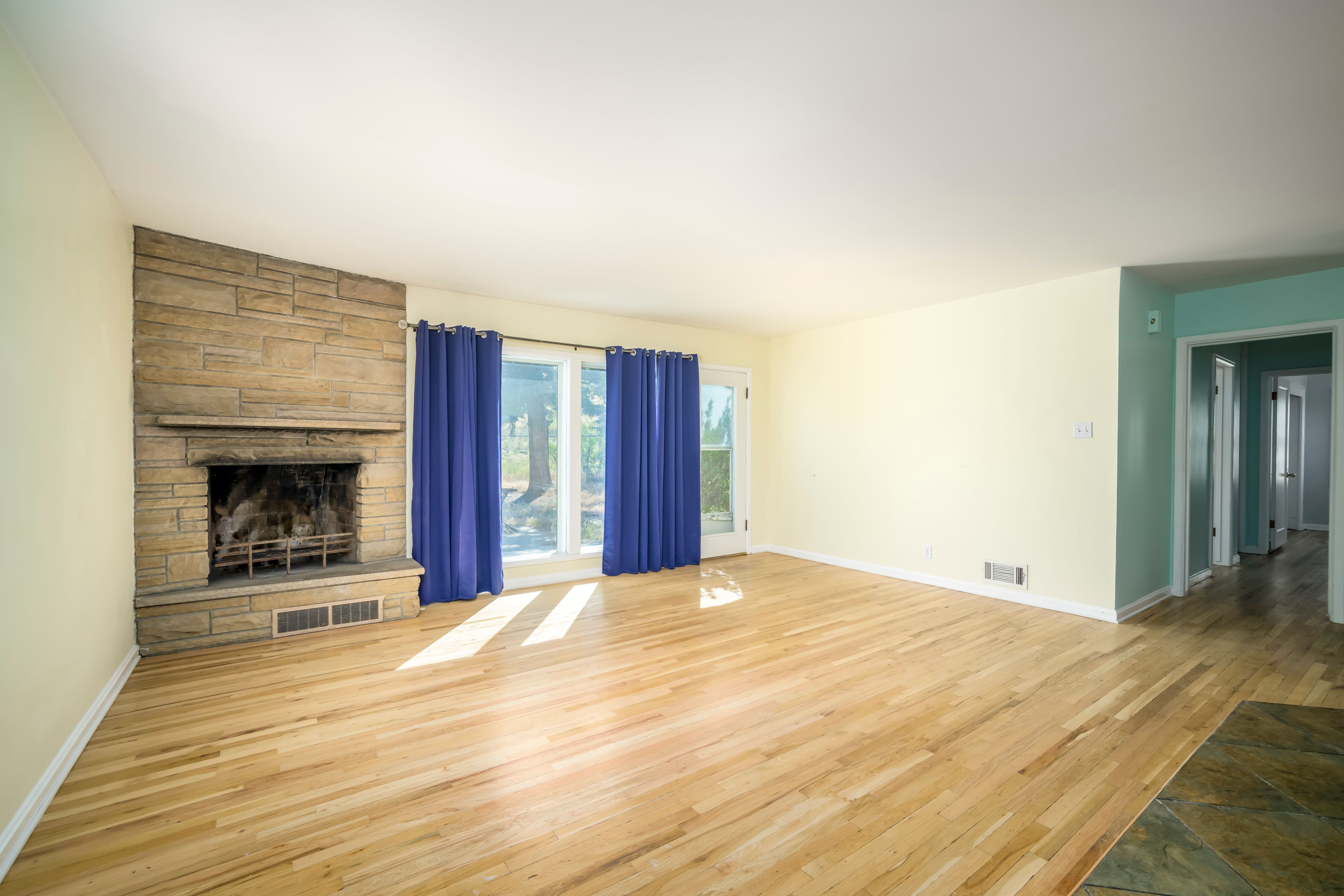 Spacious room featuring natural wood-finish flooring, a stone-faced fireplace with hearth, and large windows with exterior views