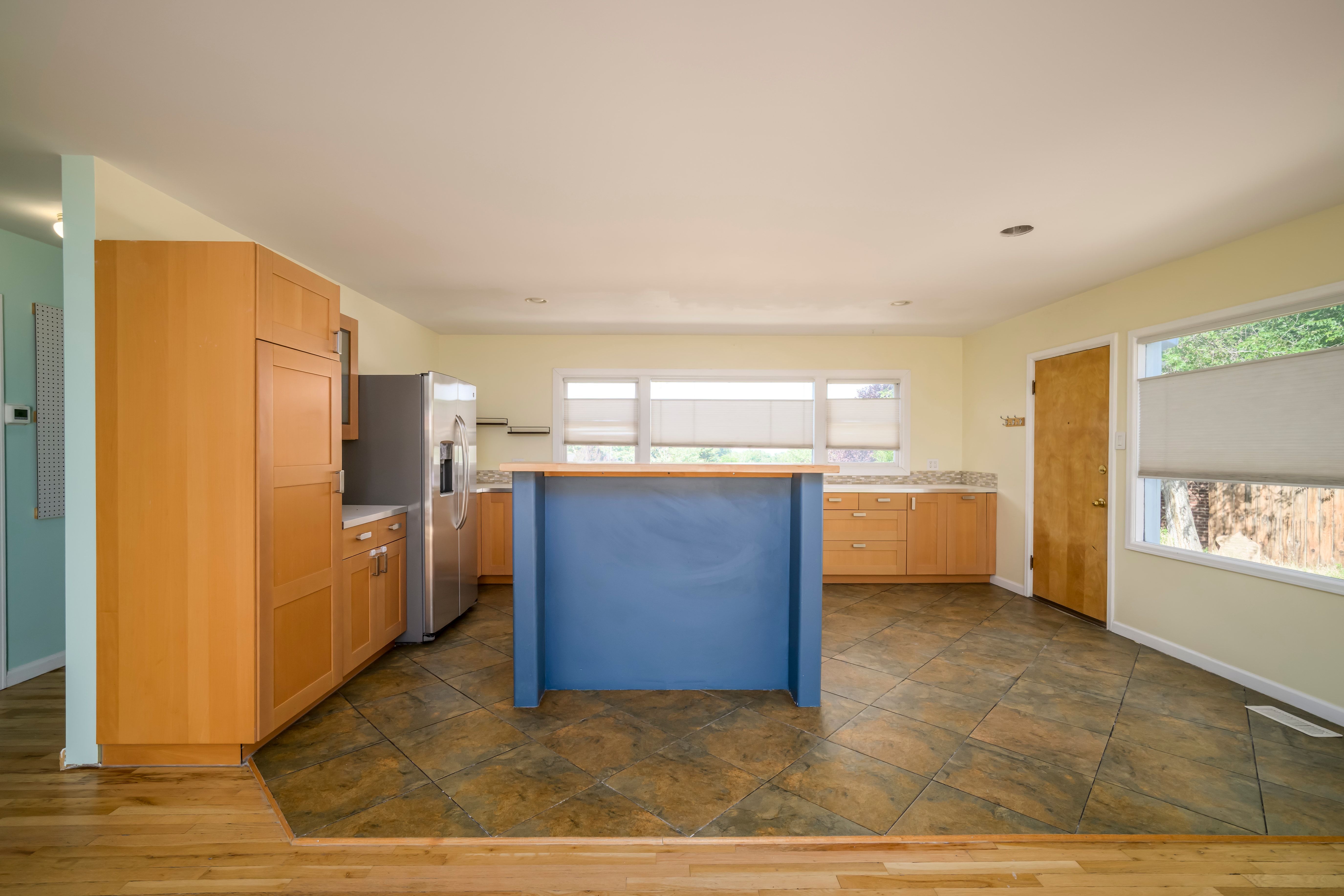 Kitchen featuring light wood cabinetry, stone-finish countertops, stainless steel refrigerator, and a blue island with a wood-finish top