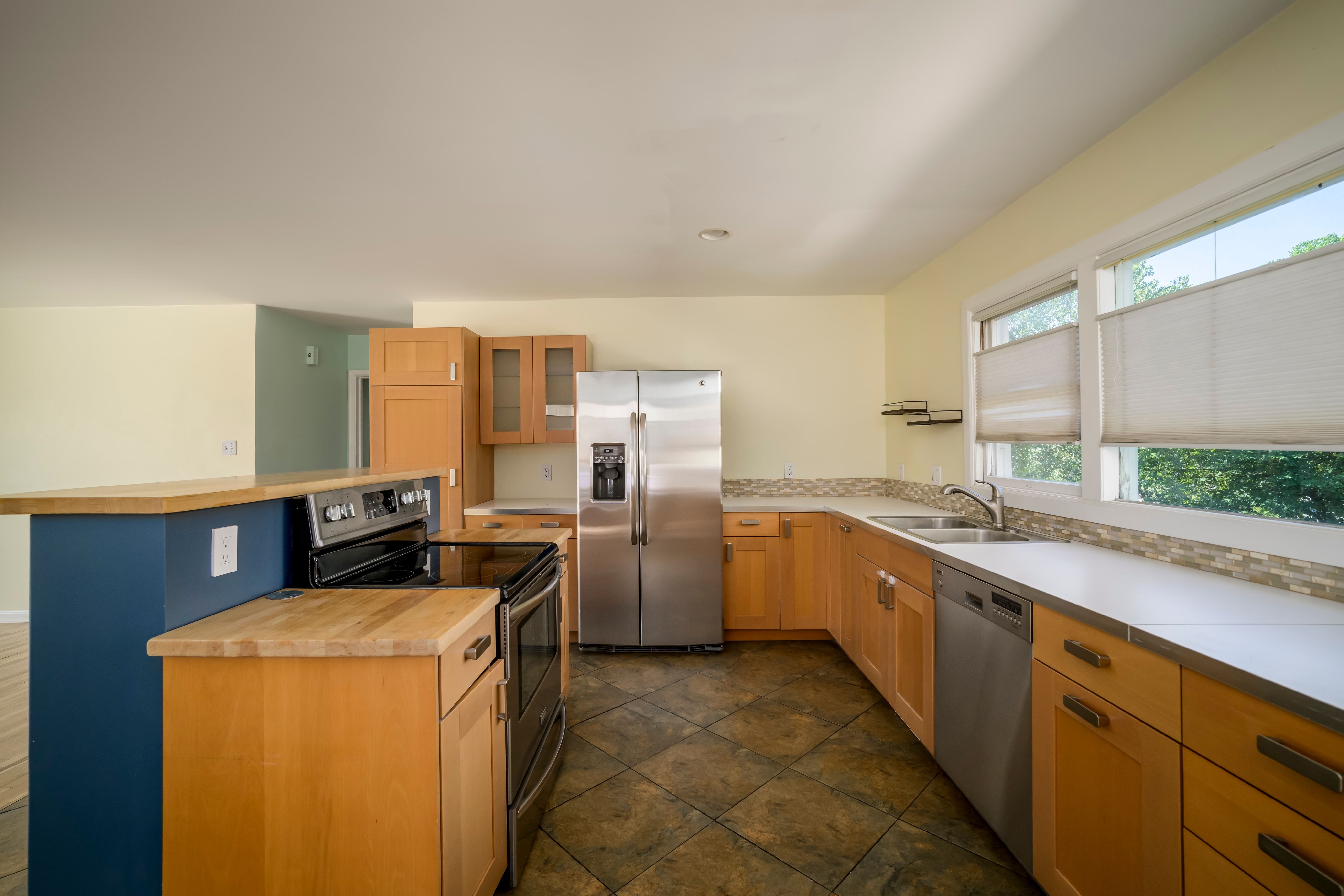 Kitchen featuring wood-finish cabinetry, stainless steel appliances, a tile backsplash, and a breakfast bar with a wood-finish countertop