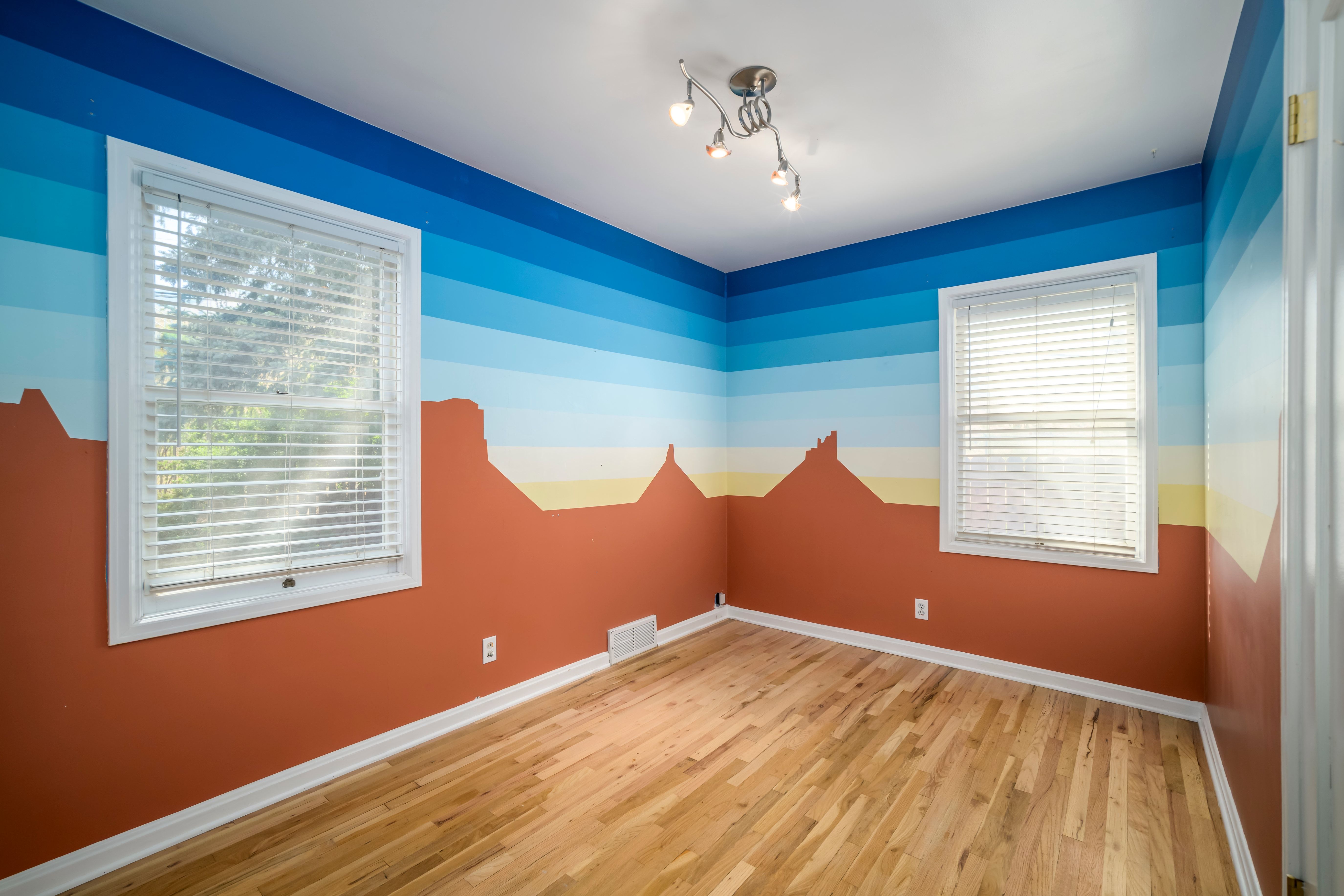 Room featuring wood-finish flooring, white baseboards, and two windows with blinds