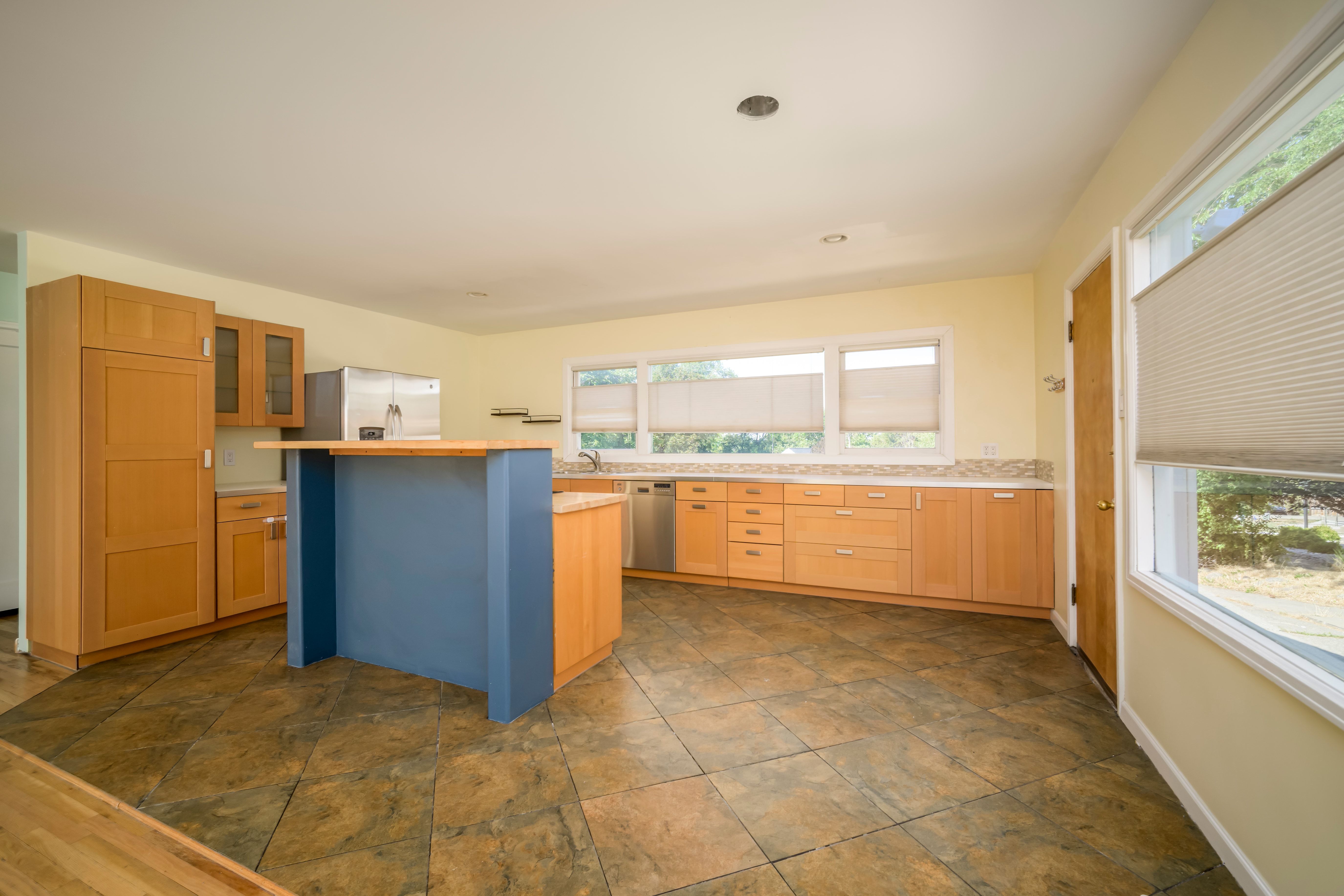 Spacious kitchen featuring large format floor tiles, light wood-finish cabinetry, a built-in refrigerator, and a central island with a breakfast bar