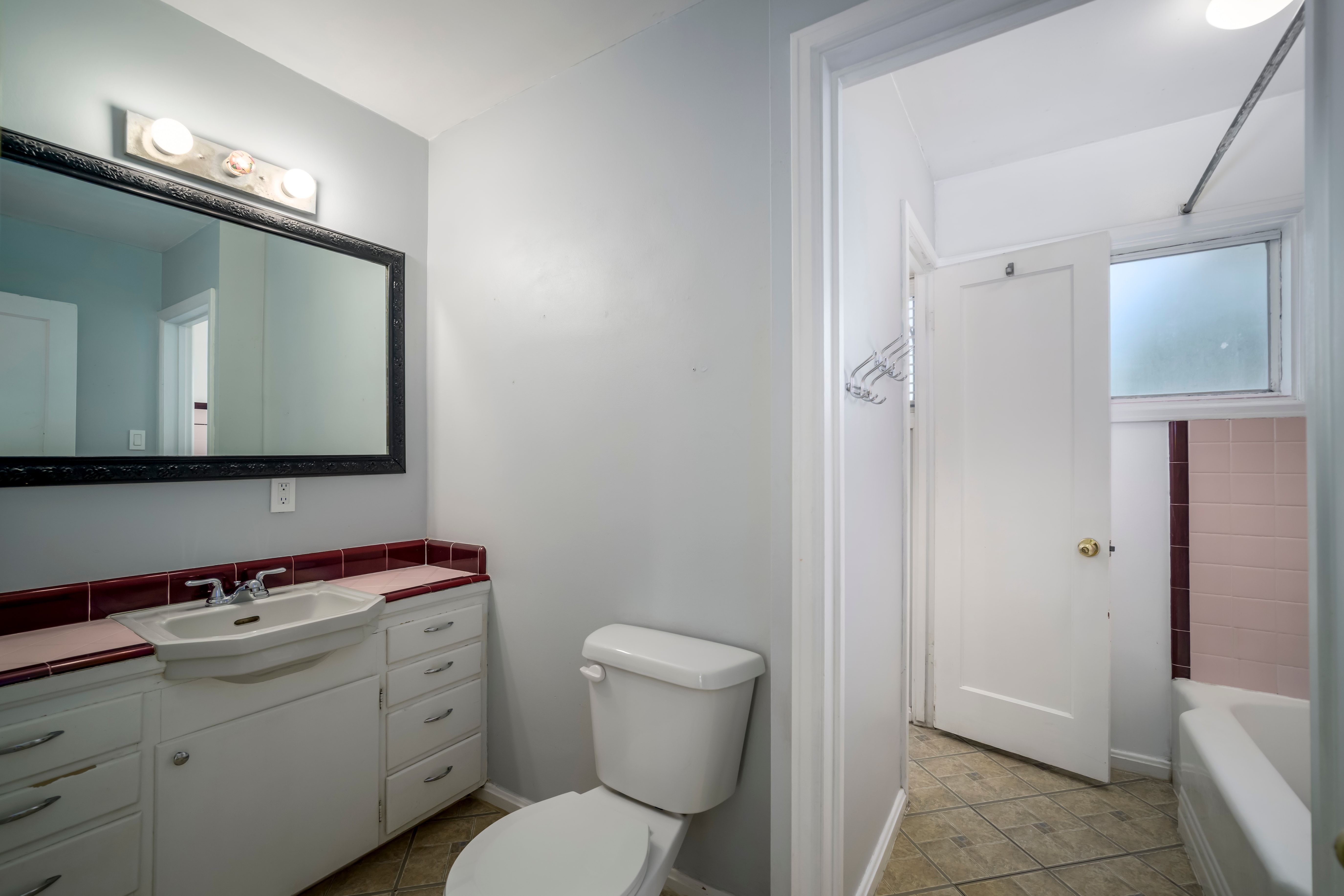 Bathroom featuring a white vanity with integrated sink, red tile countertop, and a large framed mirror