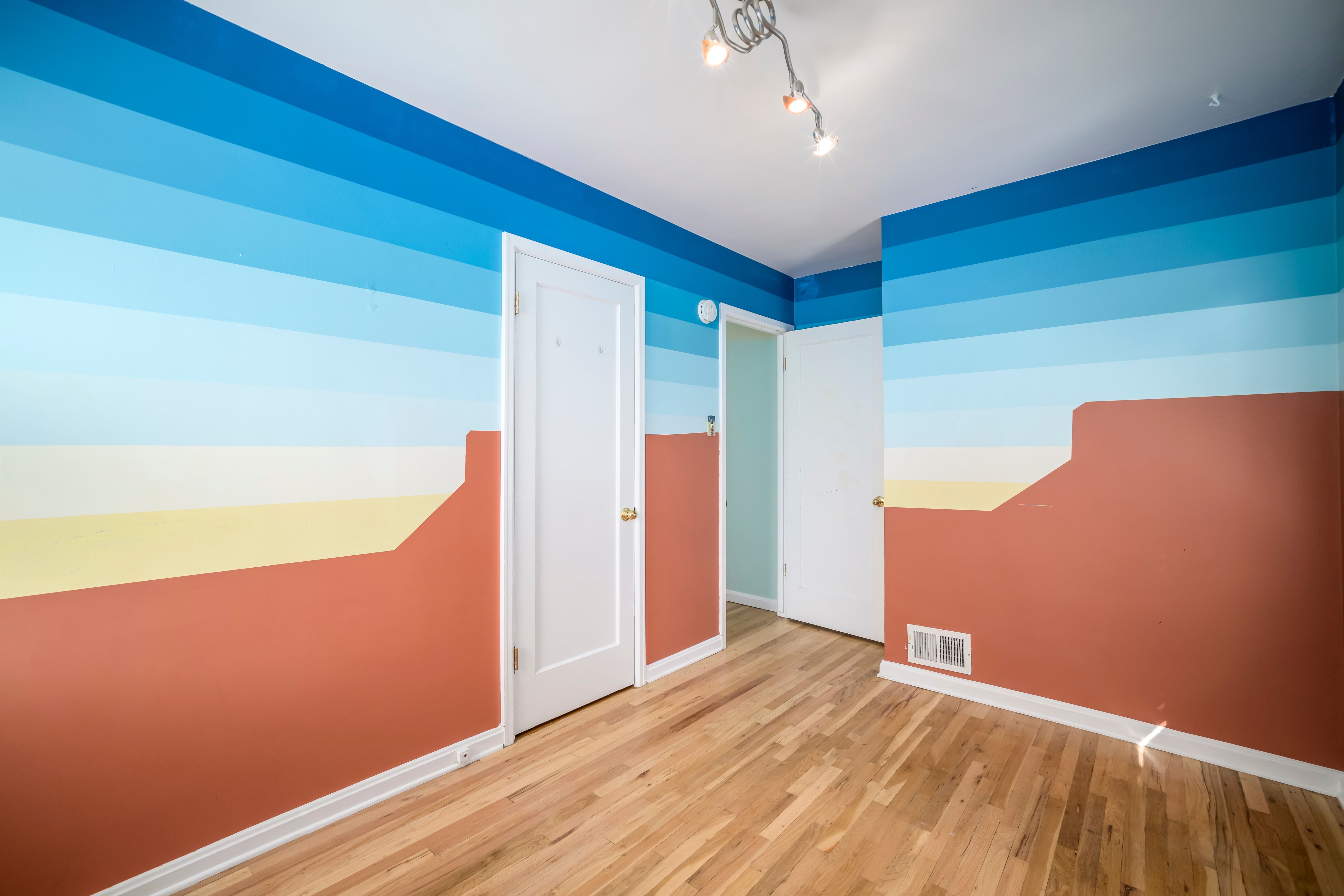 Room featuring wood-finish flooring, white baseboards, and a multi-tone painted accent wall