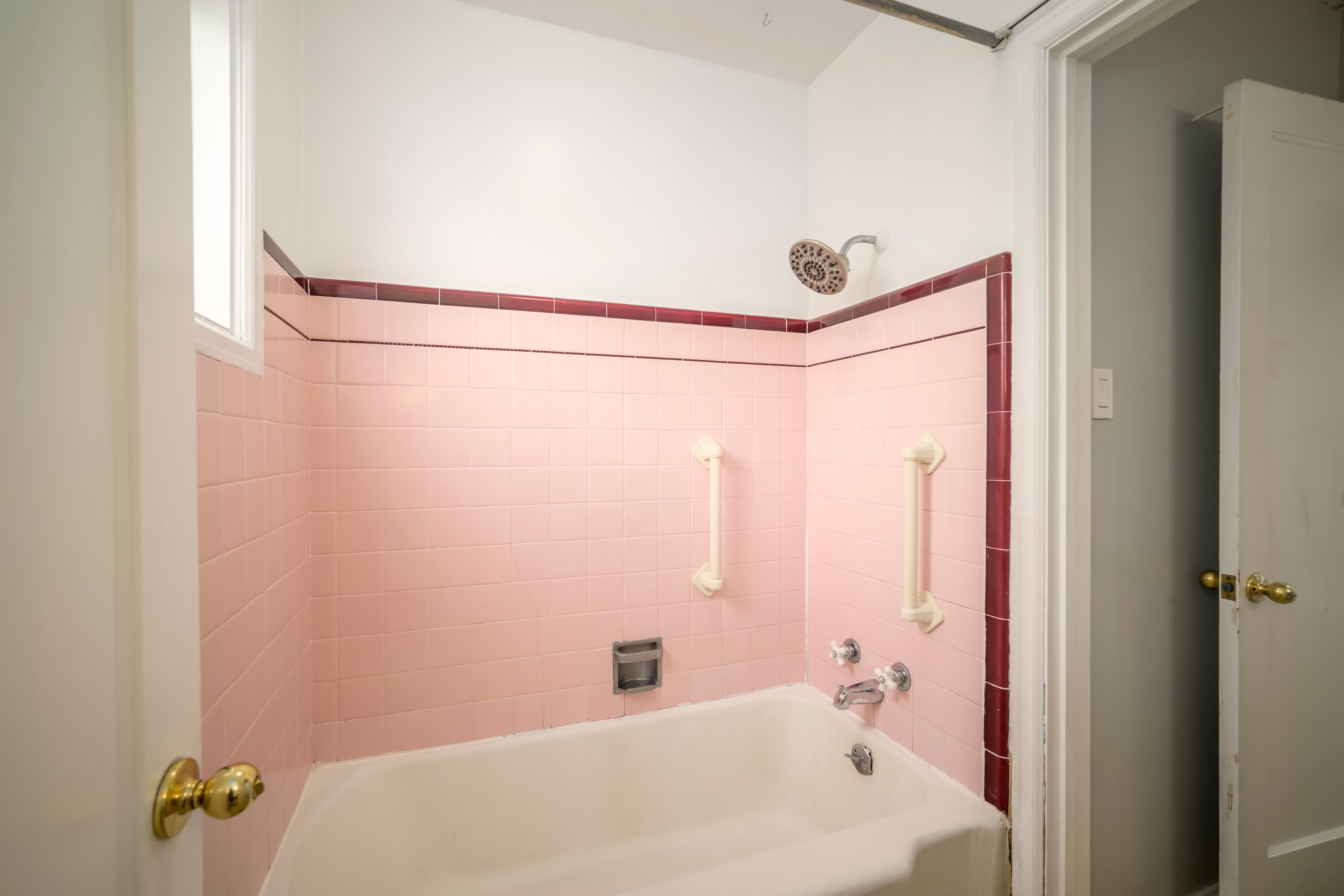 Bathtub and shower combination featuring pink tile walls with a contrasting burgundy trim