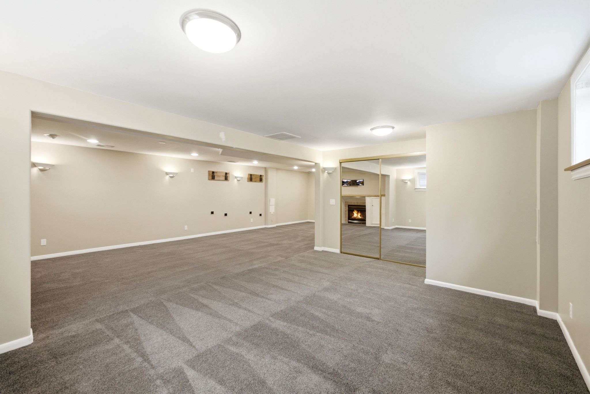 Spacious room featuring patterned gray carpeting, light-toned walls, recessed lighting, and wall sconces