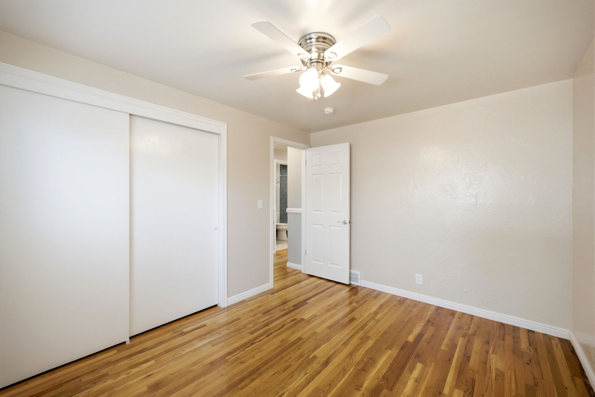 Bedroom featuring wood-finish flooring, a ceiling fan with integrated lighting, and a sliding door closet