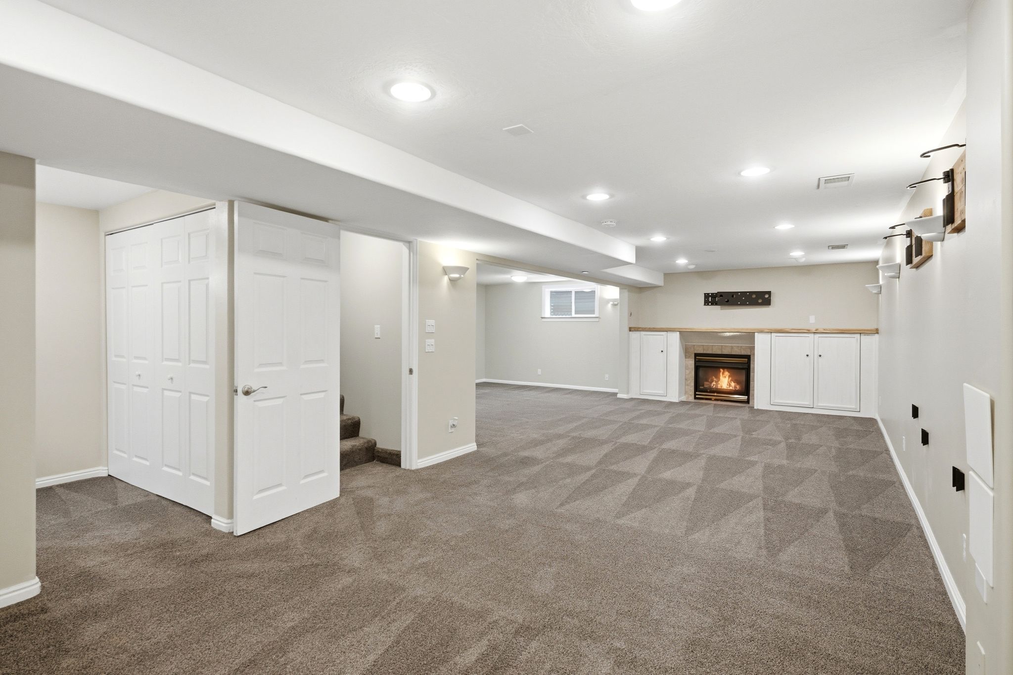 Spacious finished basement featuring patterned carpet, recessed lighting, built-in fireplace with surround cabinetry, and a window