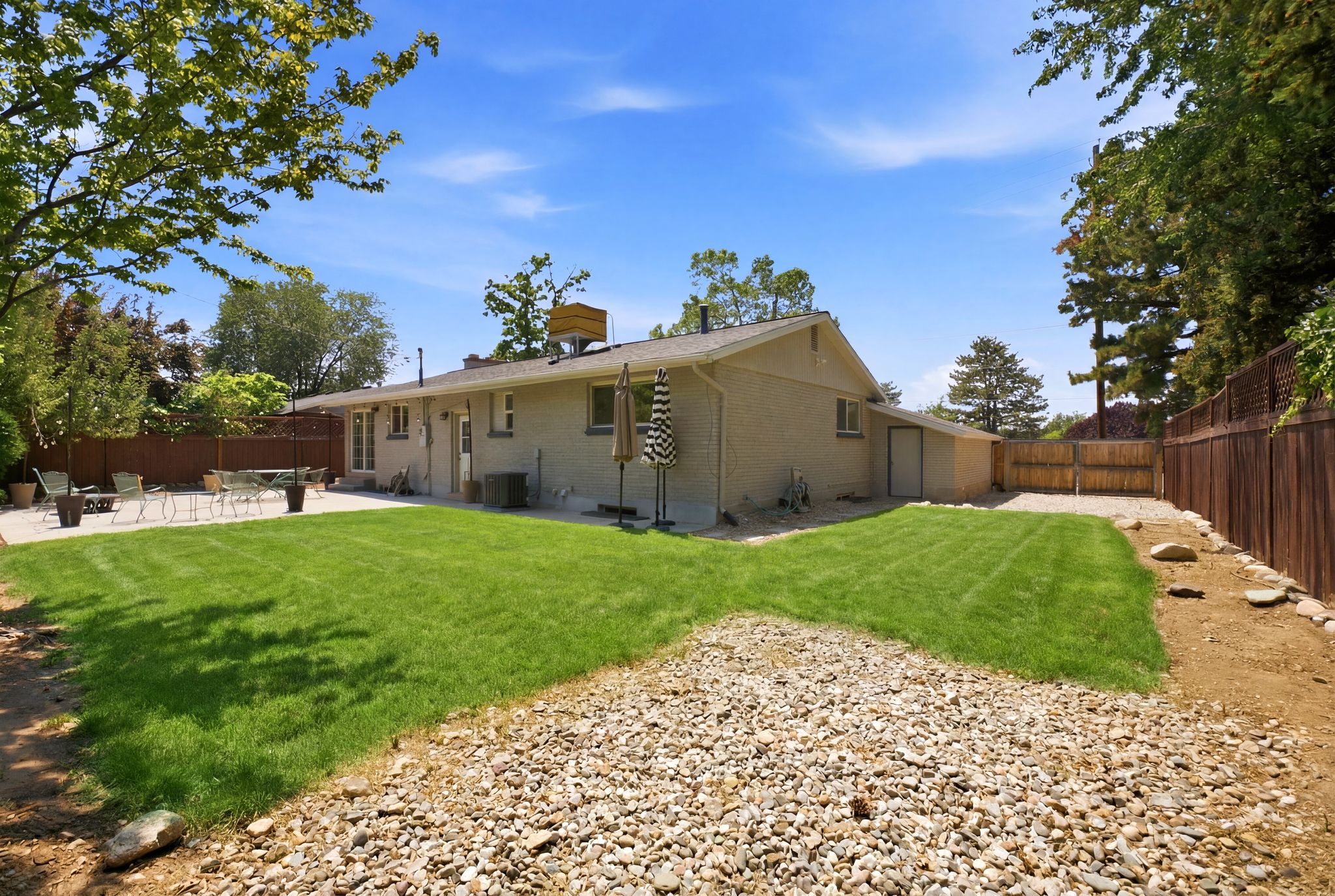 Expansive backyard with a large concrete patio, manicured lawn, and mature perimeter trees