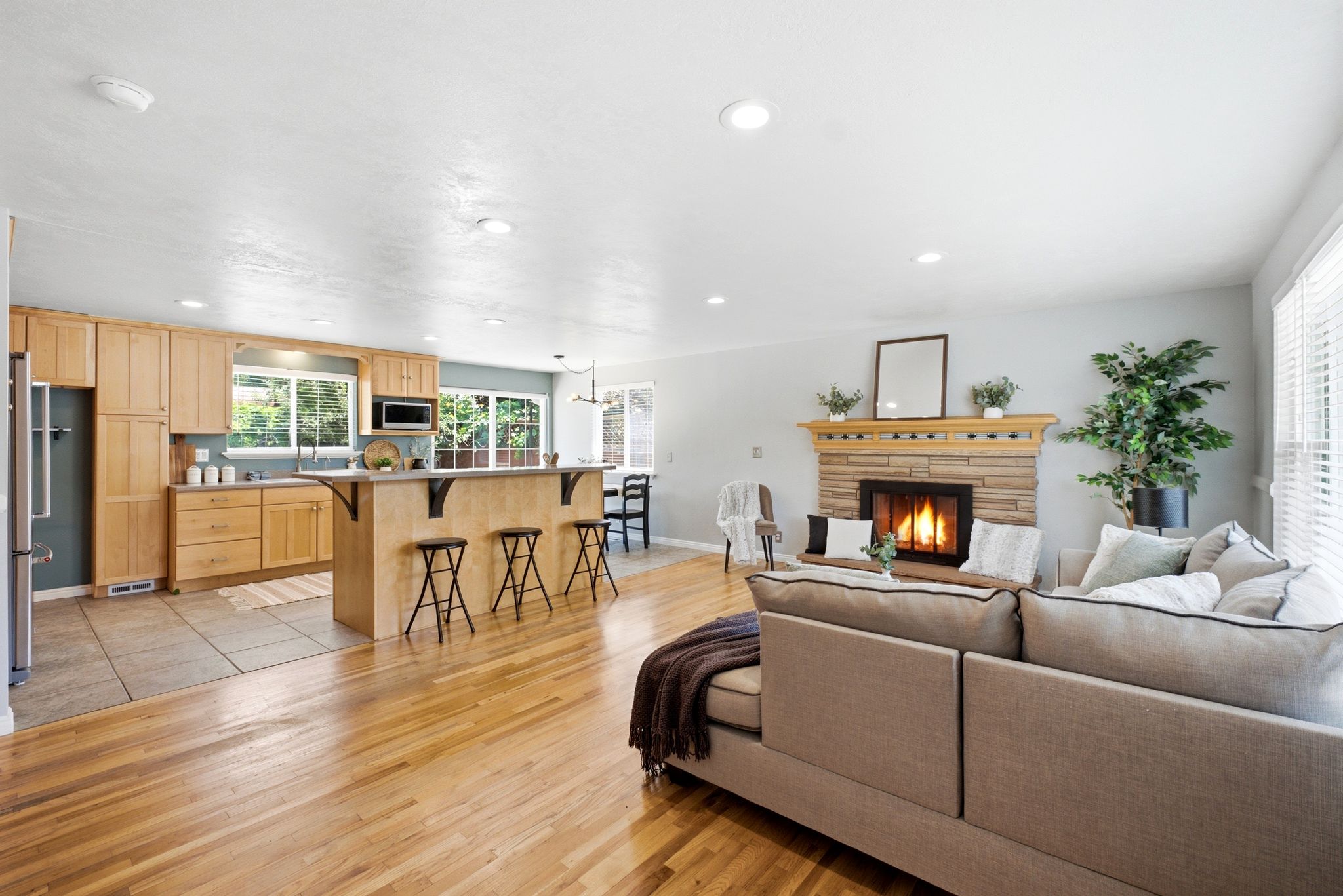 Open-concept living area featuring wood-finish flooring, a stone-surround fireplace with a wood mantle, and recessed lighting