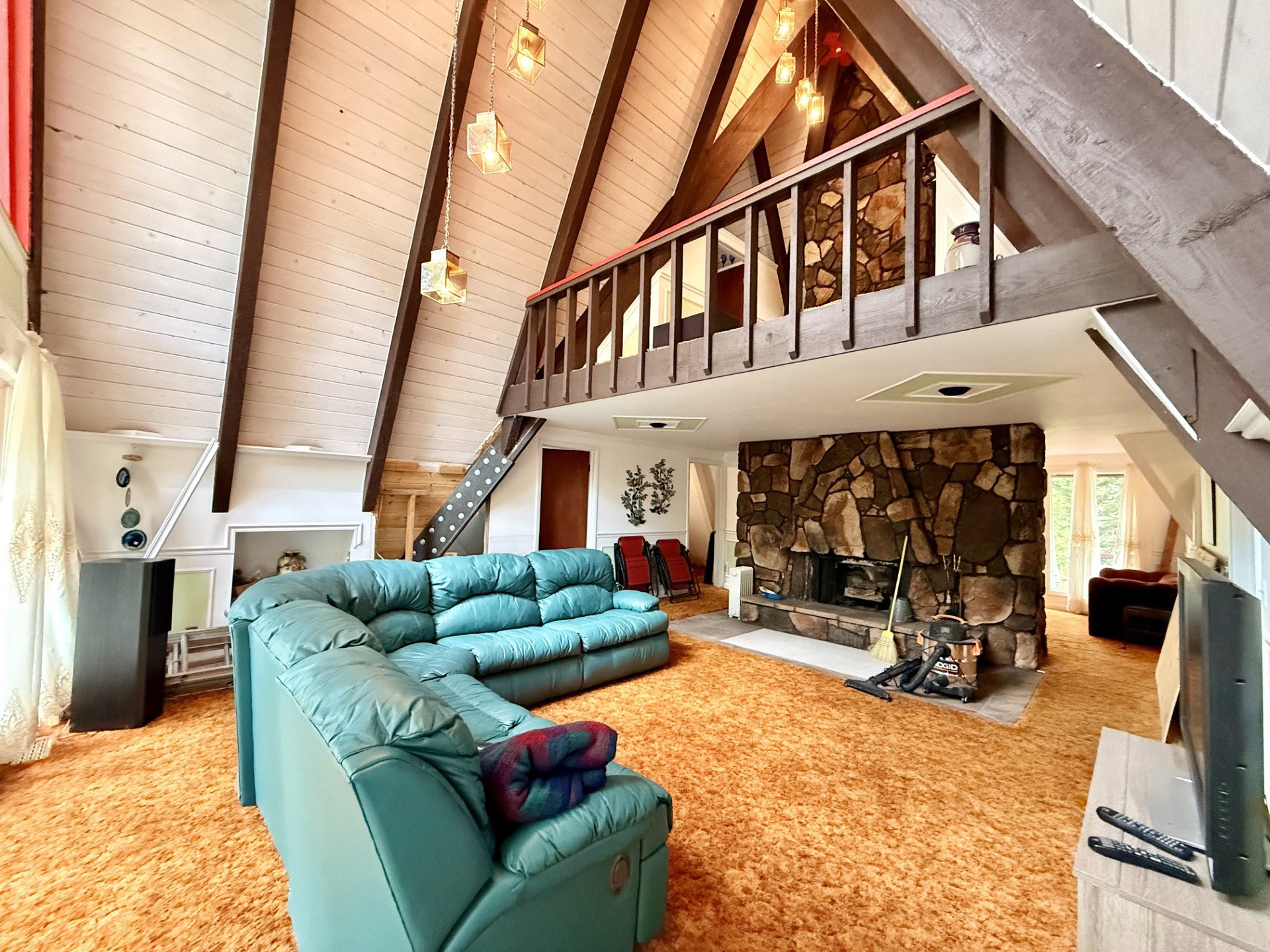 Vaulted wood-paneled ceilings with exposed beams, stone fireplace, and a loft space with wood railing