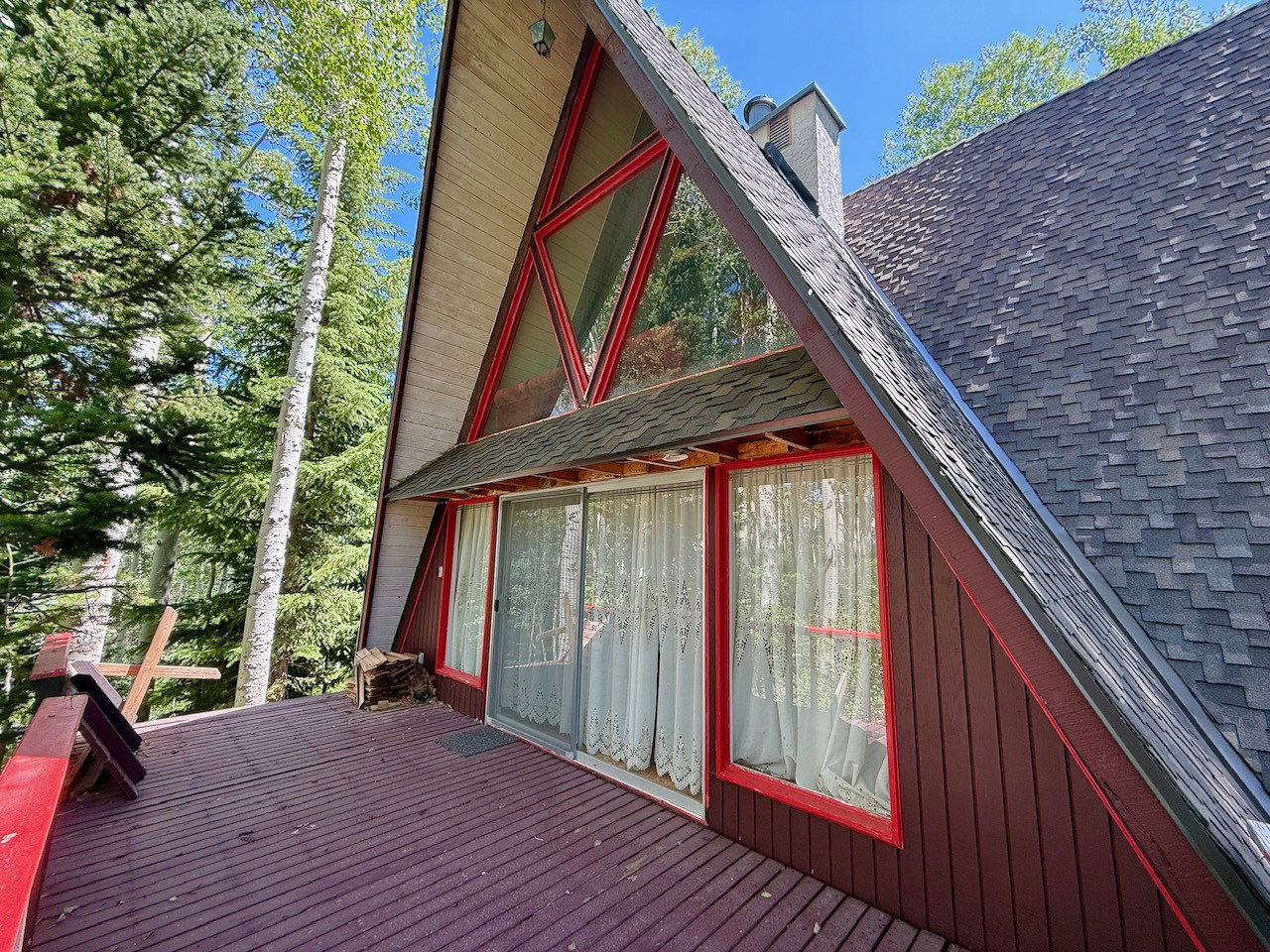 A-frame exterior featuring a prominent red-framed window wall, expansive wood deck, and a shingle roof