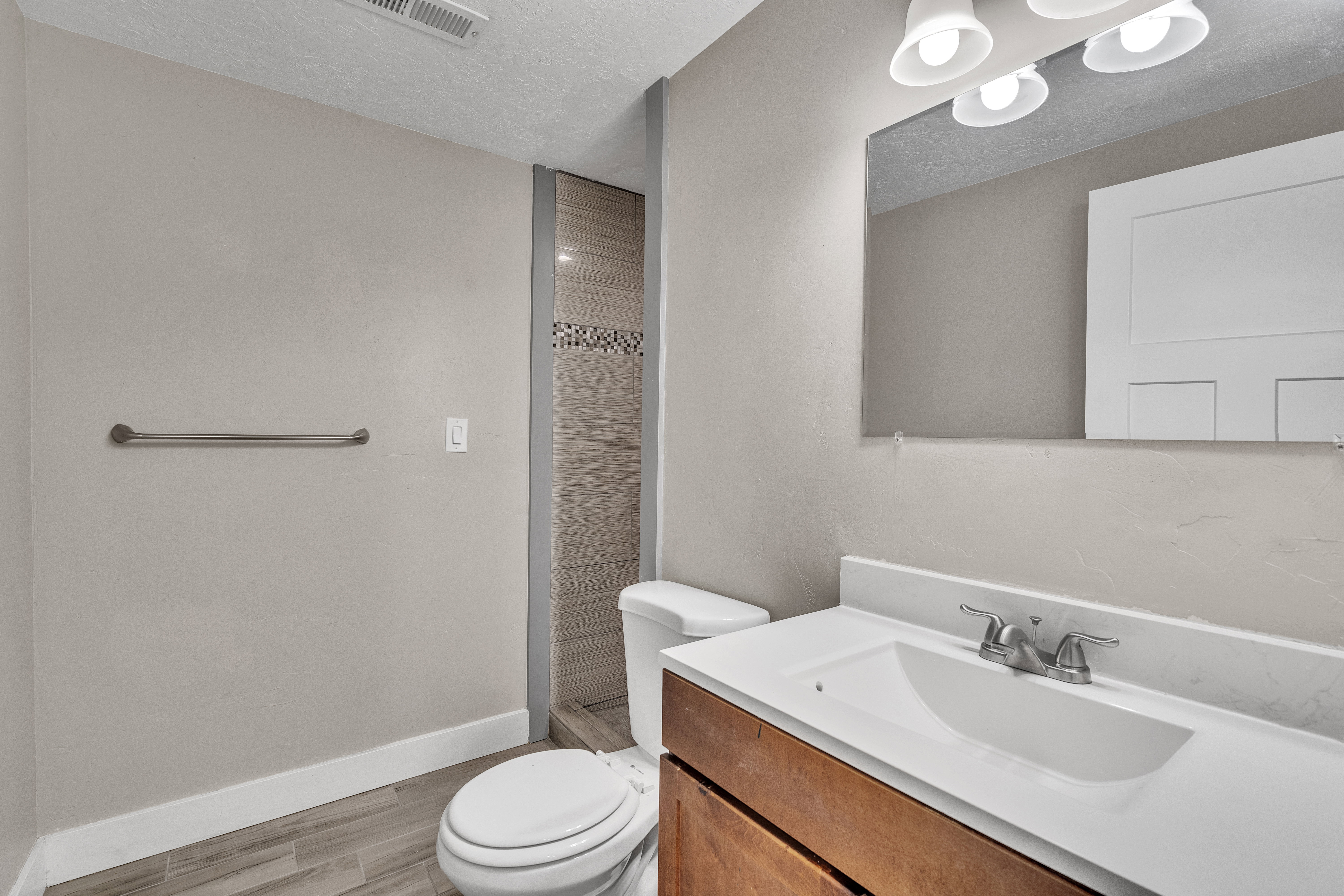 Bathroom featuring wood-finish flooring, a vanity with an integrated sink, a wall-mounted mirror, and a tiled shower with decorative accent banding