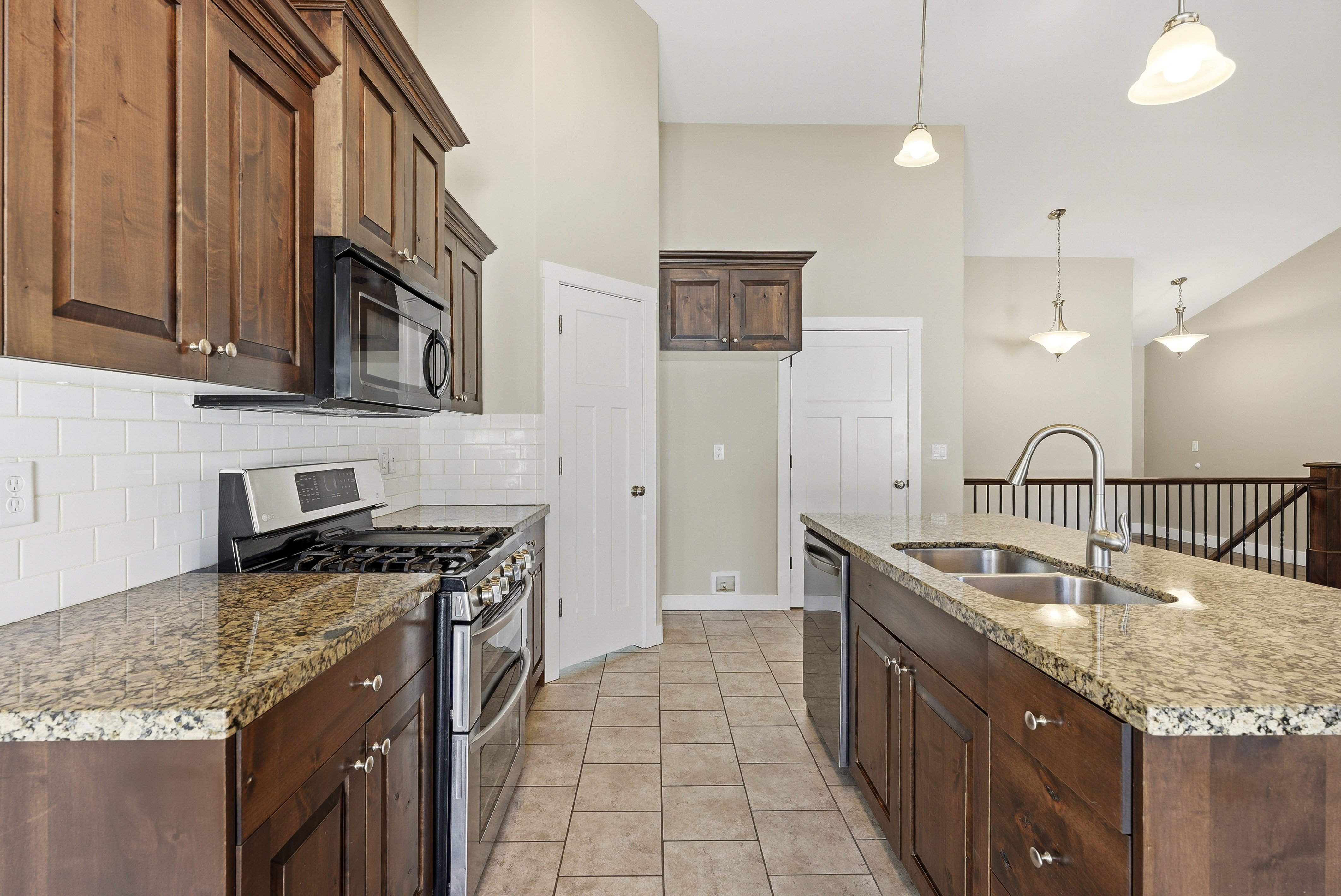 Kitchen featuring wood cabinetry,  a large pantry, stainless steel appliances, a gas range, tile backsplash, granite countertops, and a kitchen island with a dual-basin sink