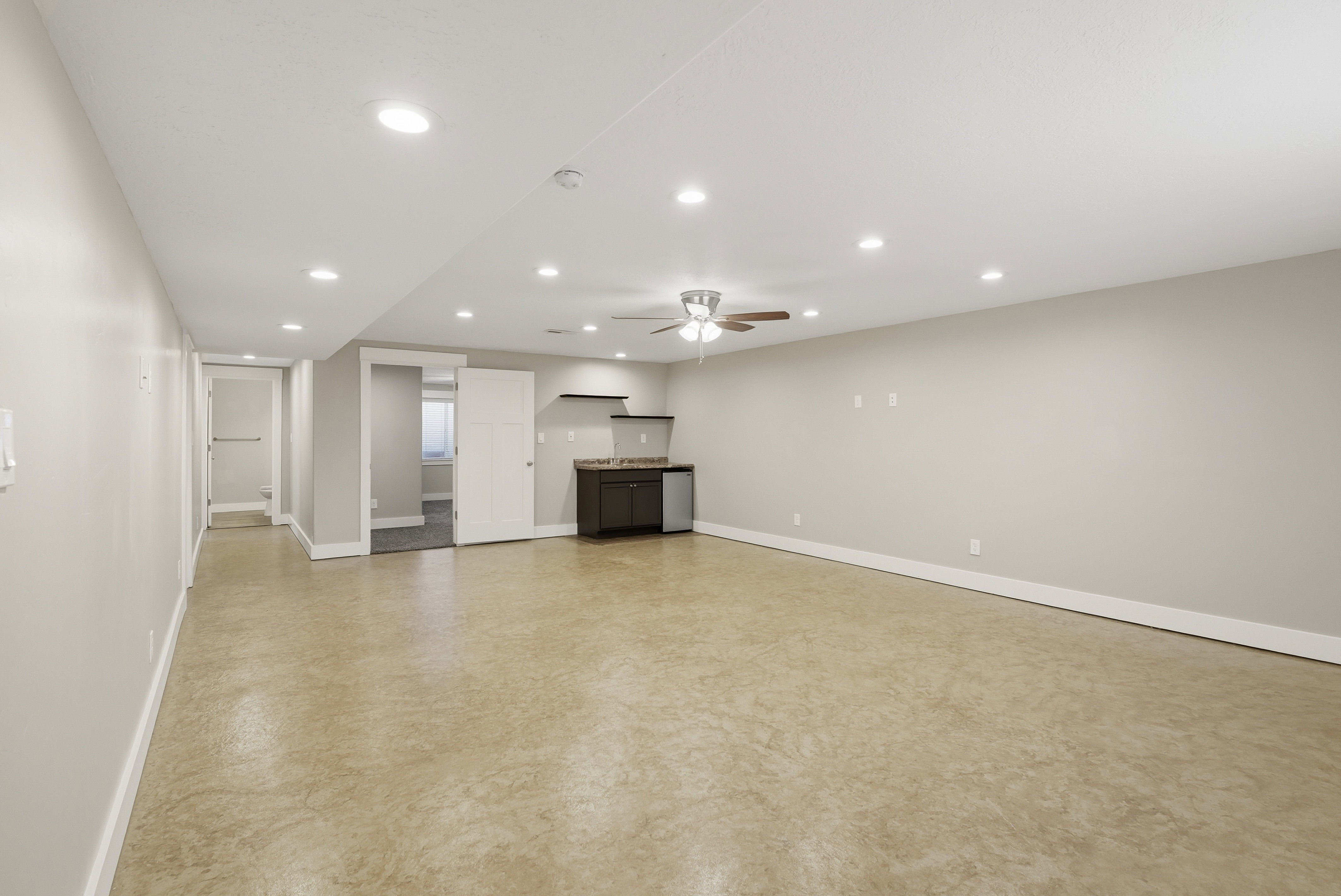 Spacious open-concept family room featuring light-toned flooring, recessed lighting, a wet bar with a space for a full-size fridge and more!