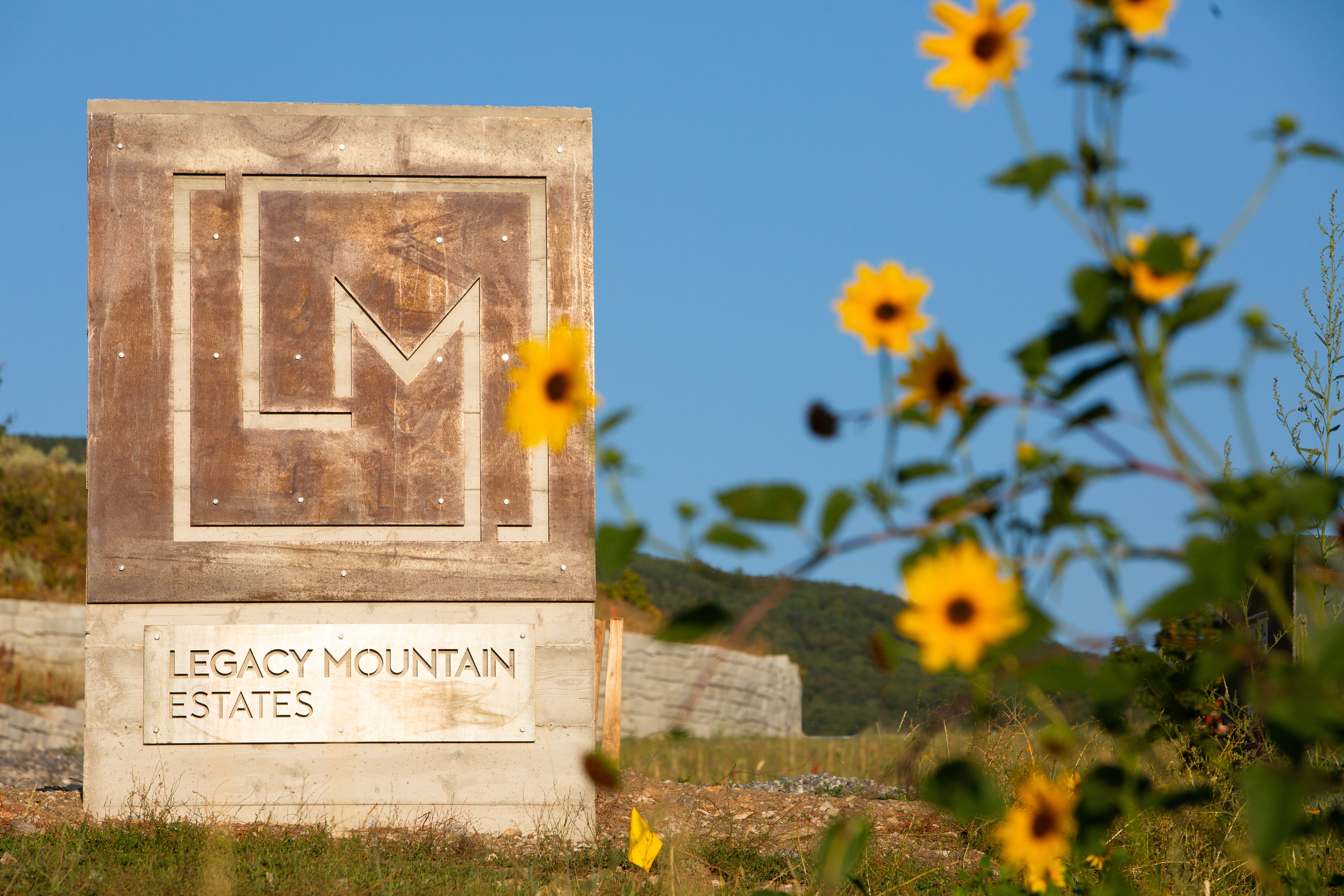 Monument sign for Legacy Mountain Estates featuring a concrete base and a weathered panel with an etched "LM" design