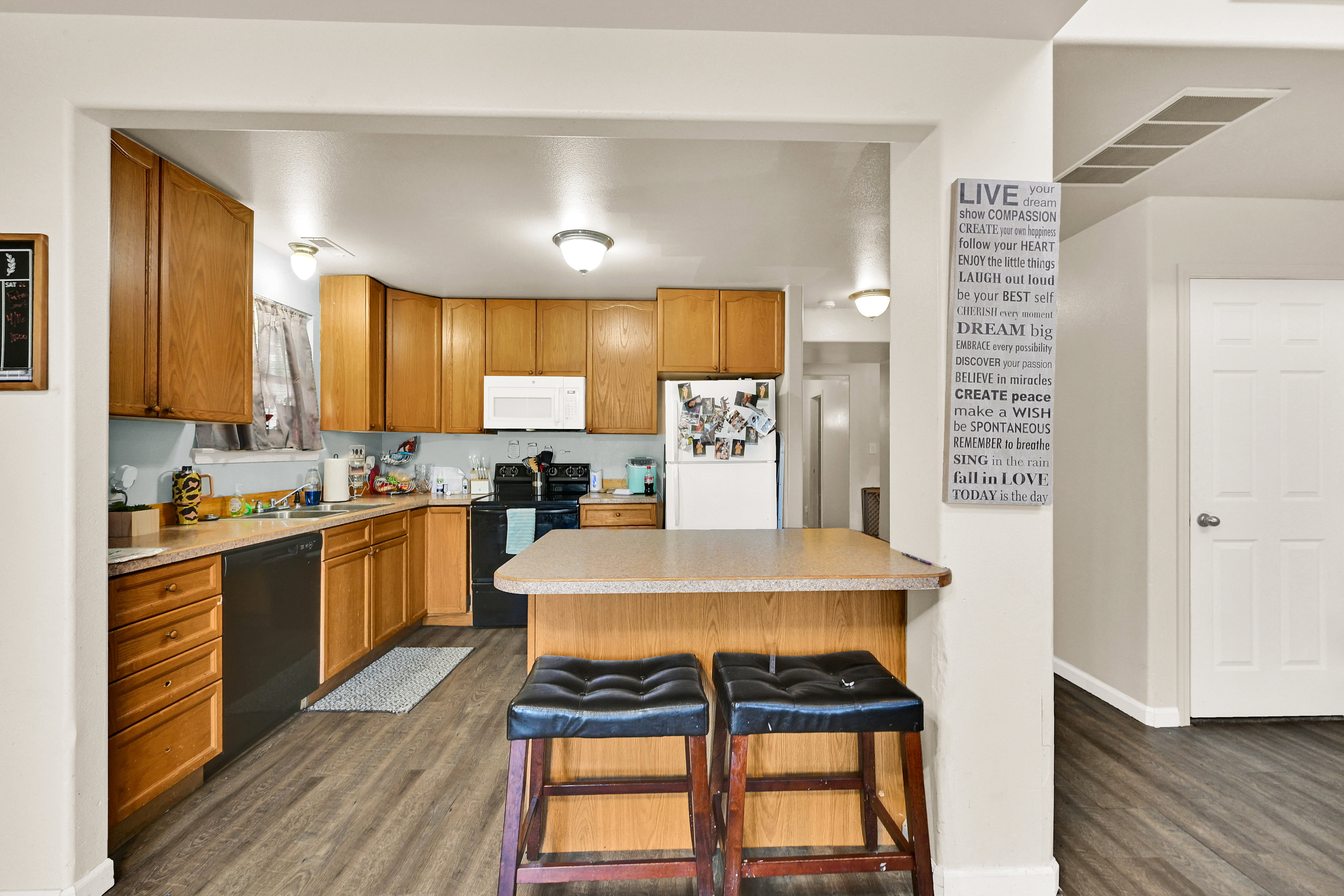 Kitchen featuring wood-finish cabinetry, black appliances, light-toned countertops, a breakfast bar, and wood-look flooring