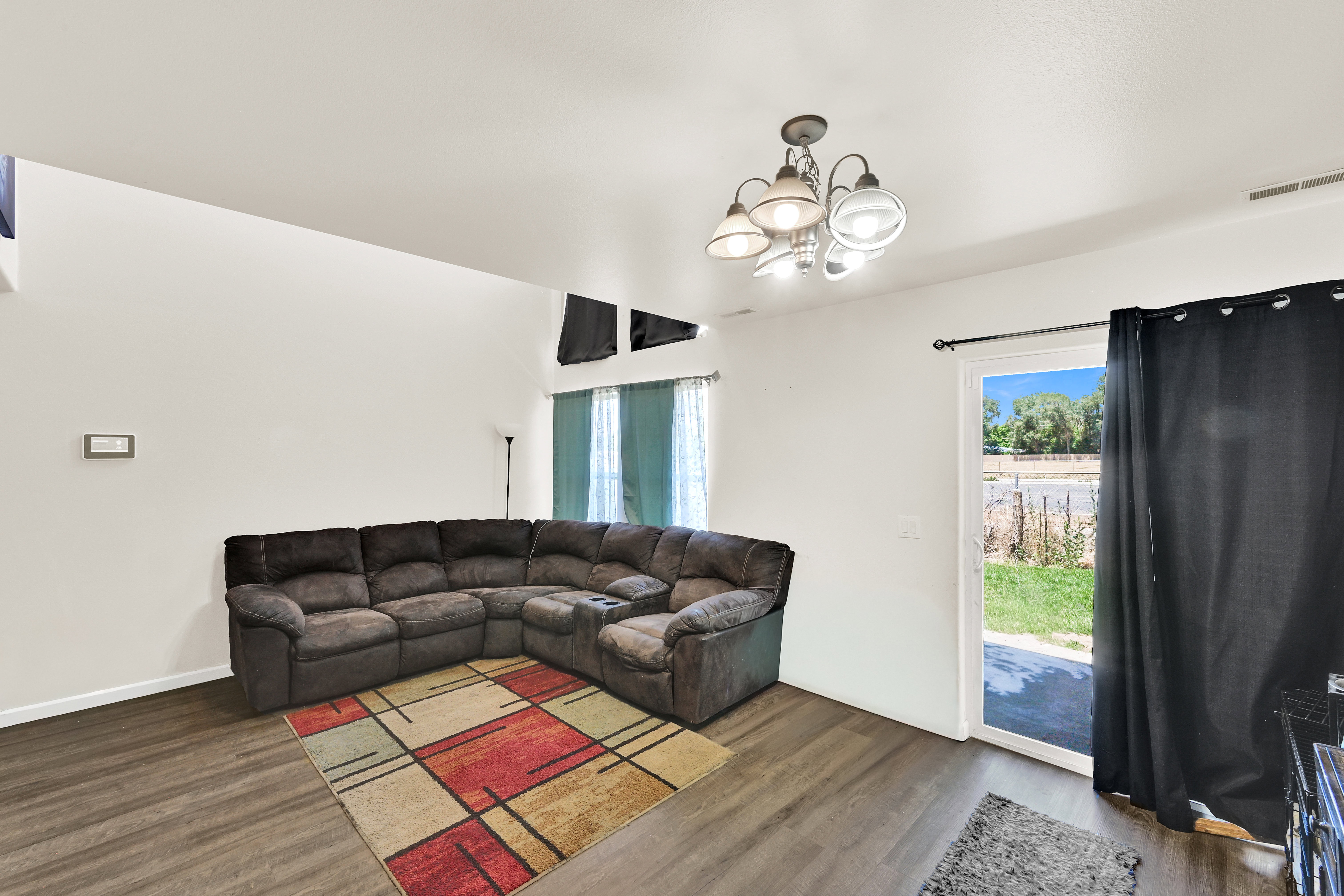 Spacious living area featuring wood-finish flooring, a contemporary ceiling light fixture, and a sliding glass door providing exterior access