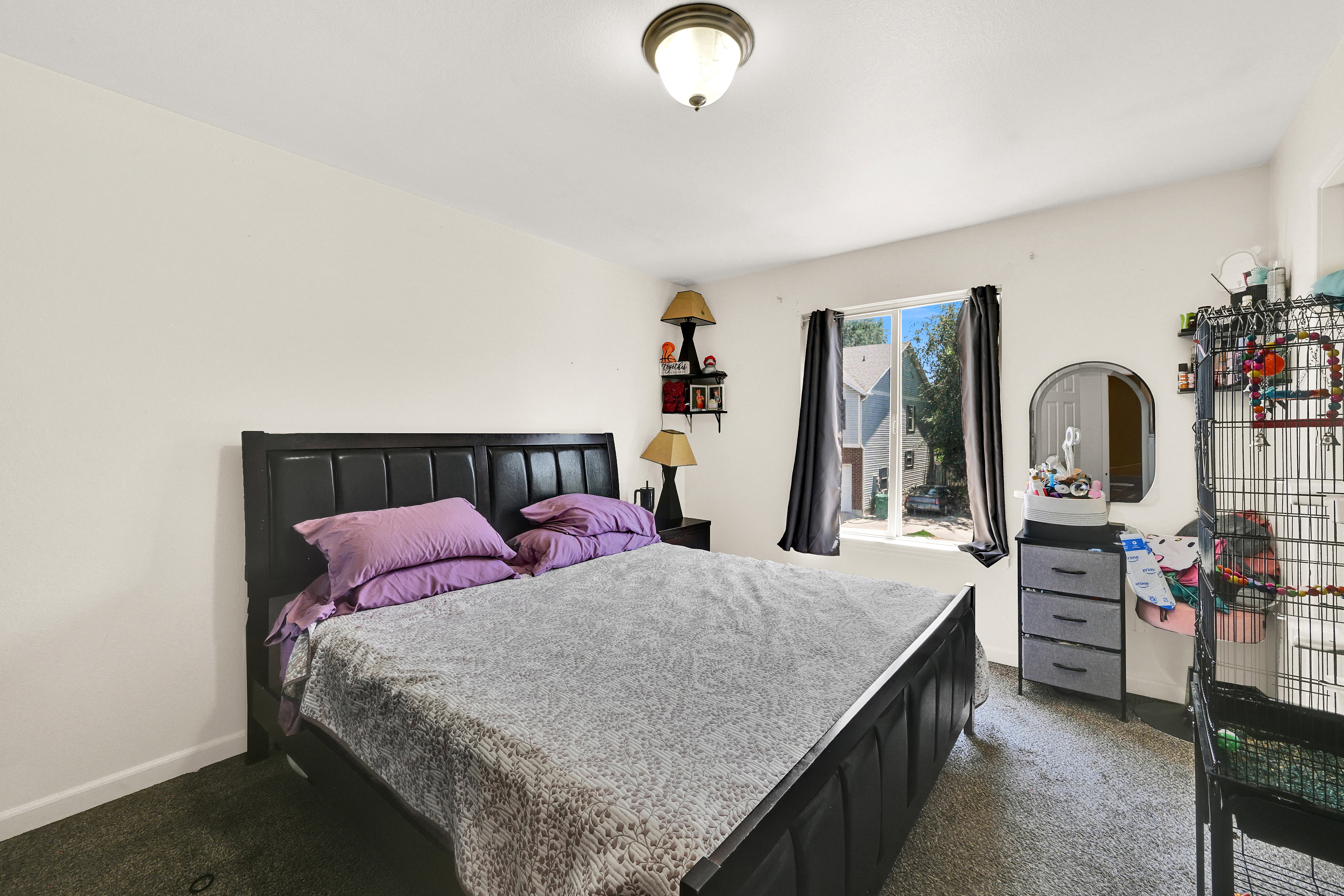Carpeted bedroom with a single window featuring dark drapes