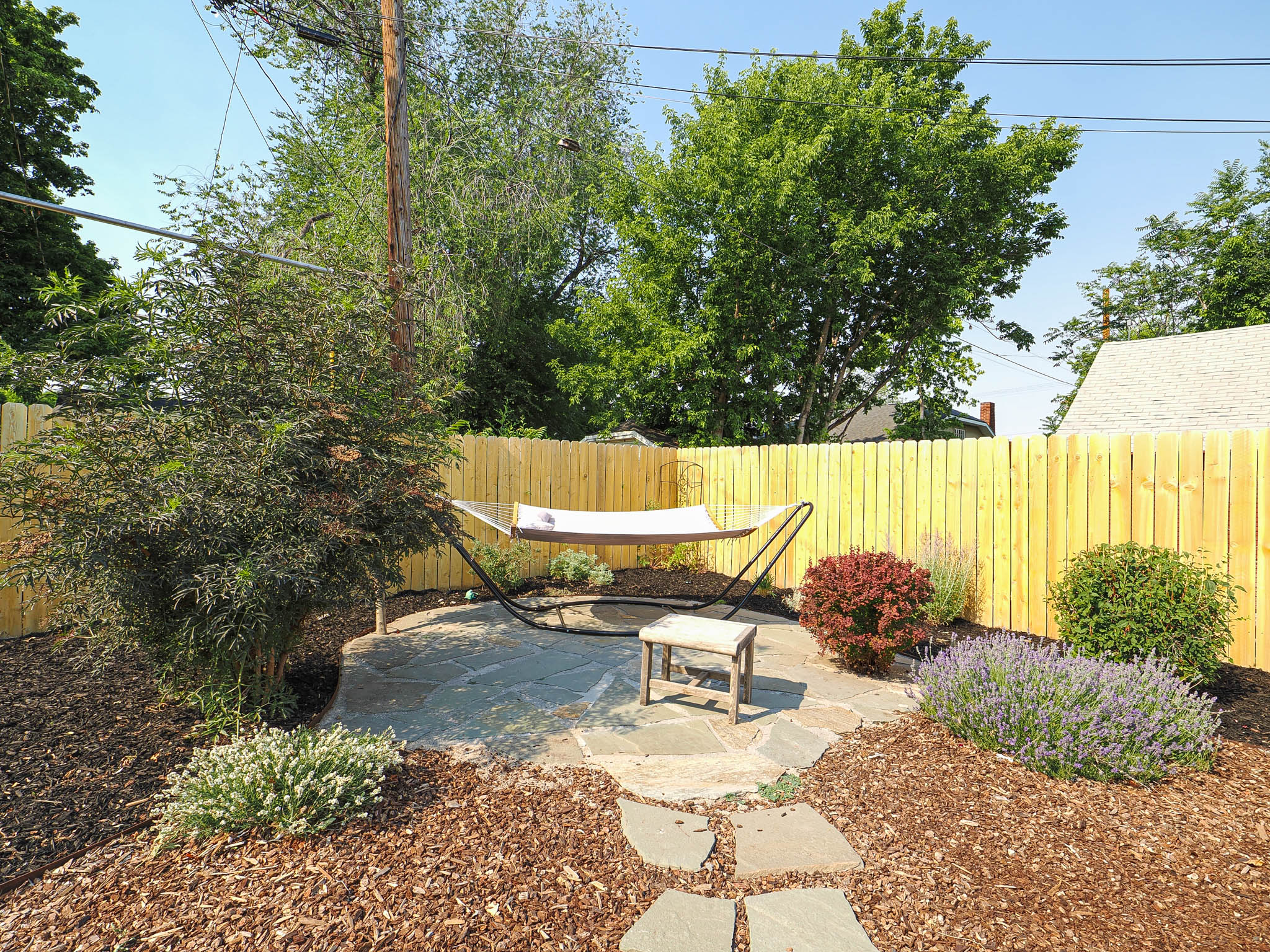 Private backyard retreat featuring a flagstone patio, lush landscaping with flowering shrubs, and a wood privacy fence