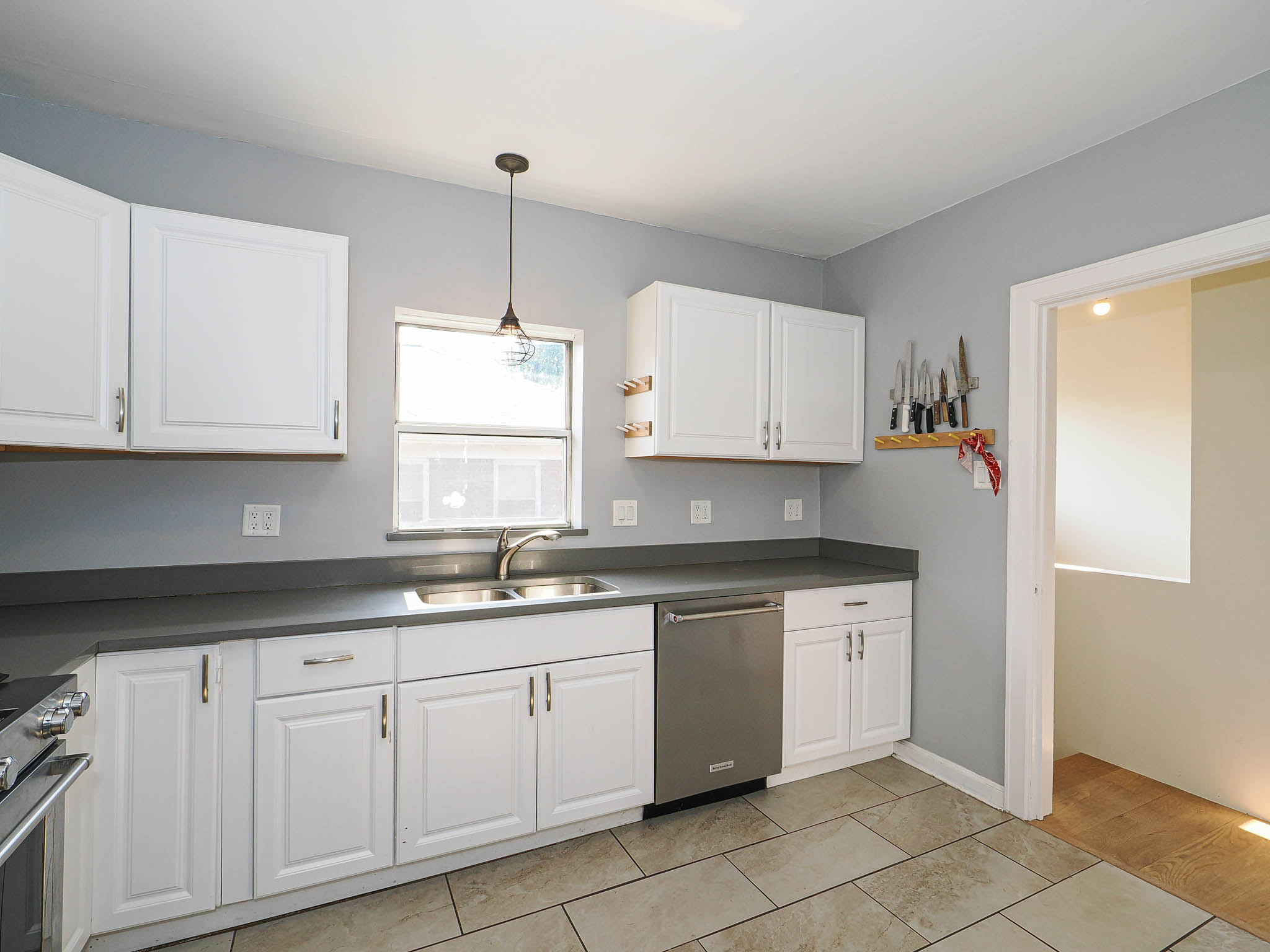 Kitchen featuring white shaker-style cabinetry, dark countertops, a double basin stainless steel sink, and a stainless steel dishwasher