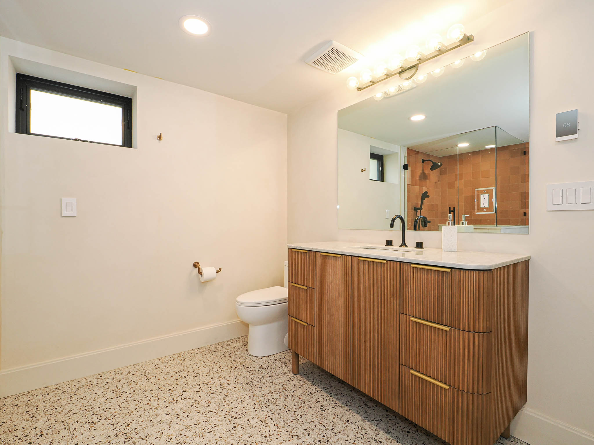 Bathroom featuring a wood-finish vanity with gold-tone hardware, a white countertop with an undermount sink, a large wall-mounted mirror, and speckled flooring