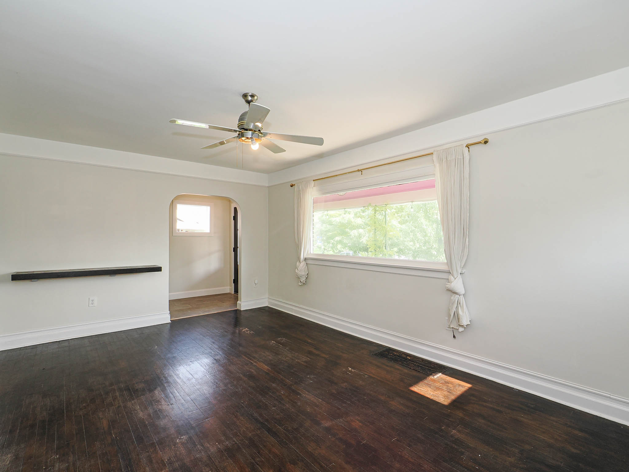 Spacious room featuring dark wood-finish flooring, white baseboards, and a contemporary ceiling fan