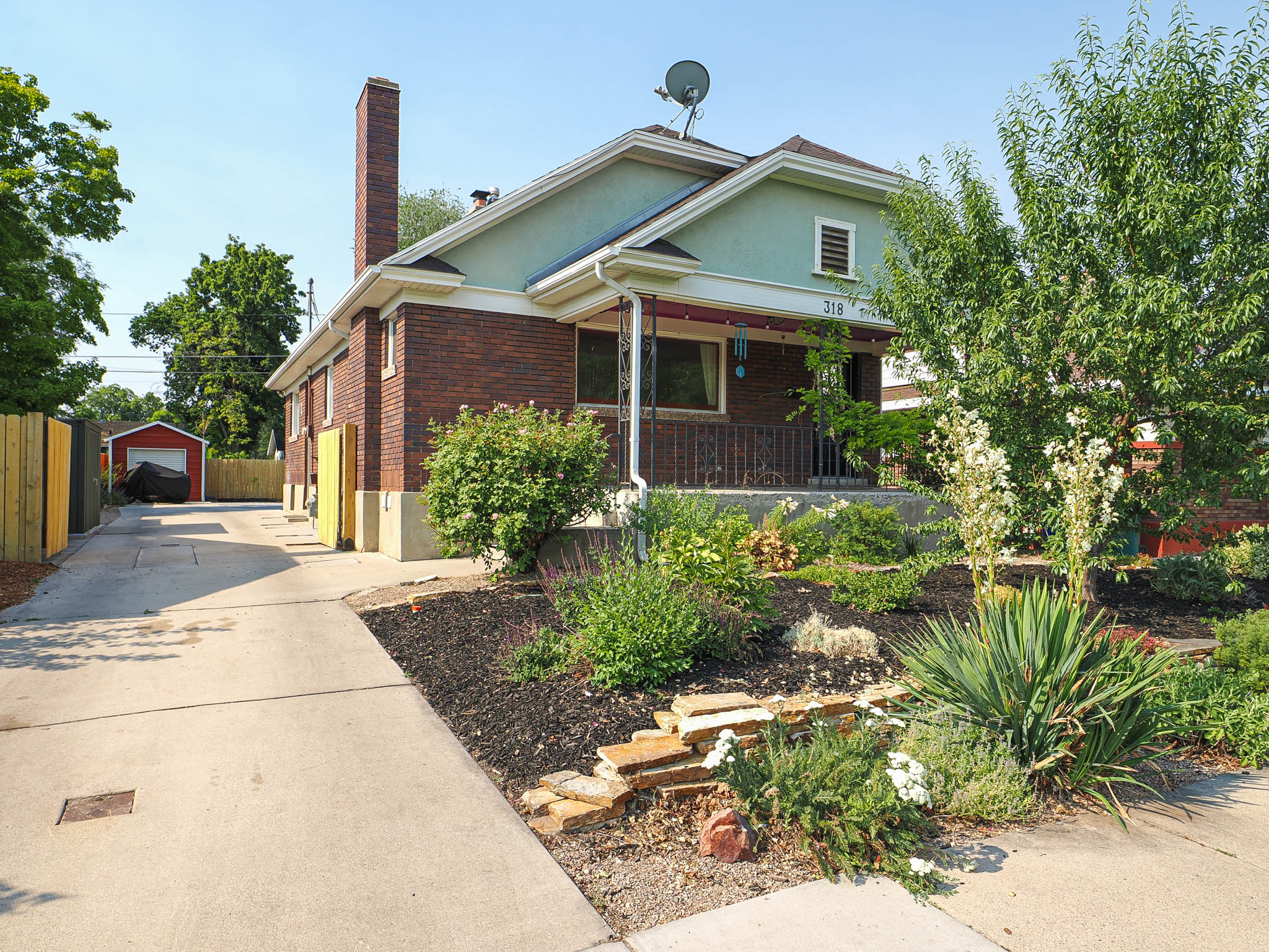 Brick-sided residence featuring a landscaped front yard with varied plantings and stone accents
