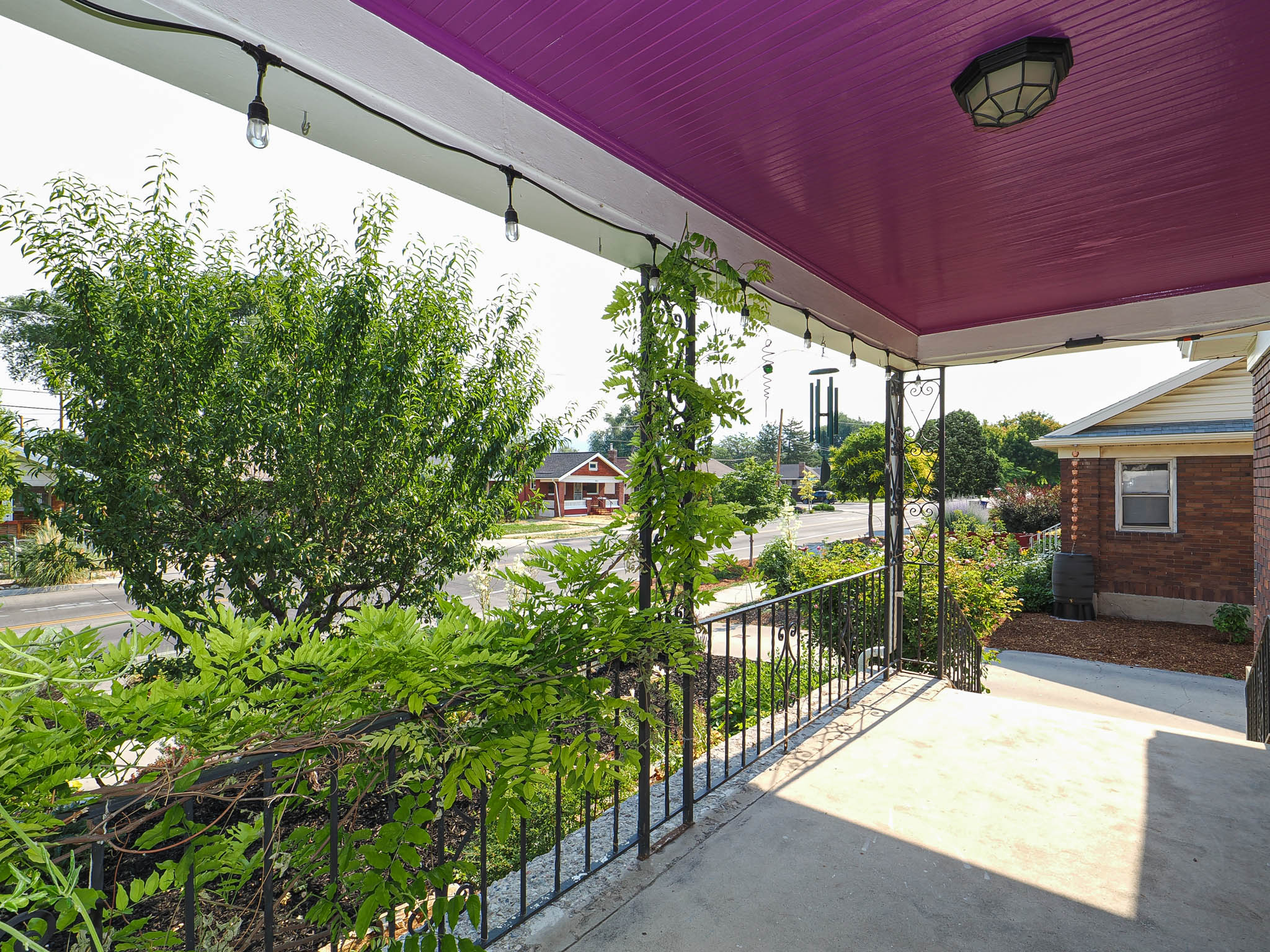 Front porch featuring a concrete surface, wrought iron railing, string lighting, and a vibrant purple ceiling