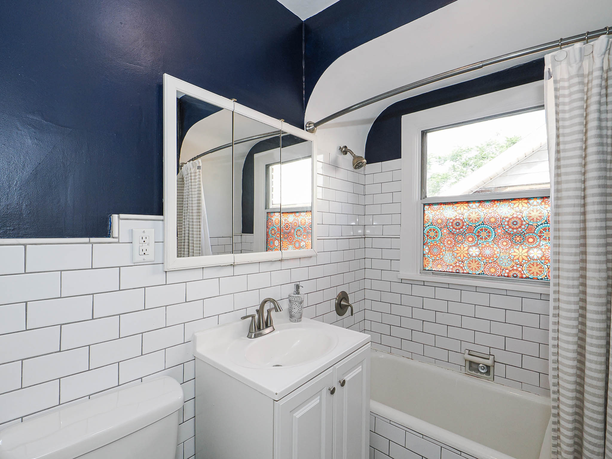 Bathroom featuring white subway tile surround, white vanity with integrated sink, brushed nickel faucet, and a medicine cabinet with mirrored doors