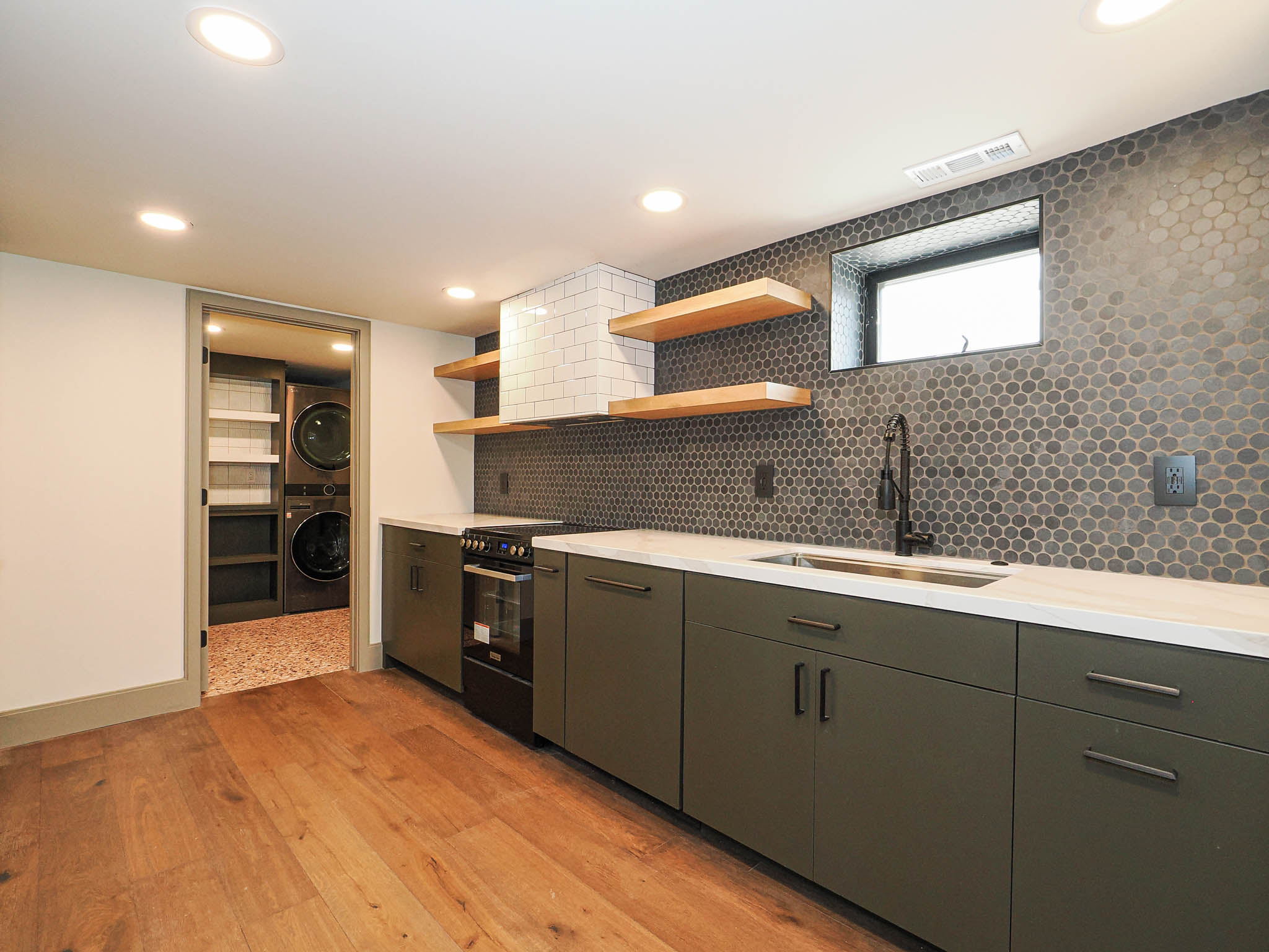 Modern kitchenette featuring dark green cabinetry, white countertops, and a gray penny tile backsplash