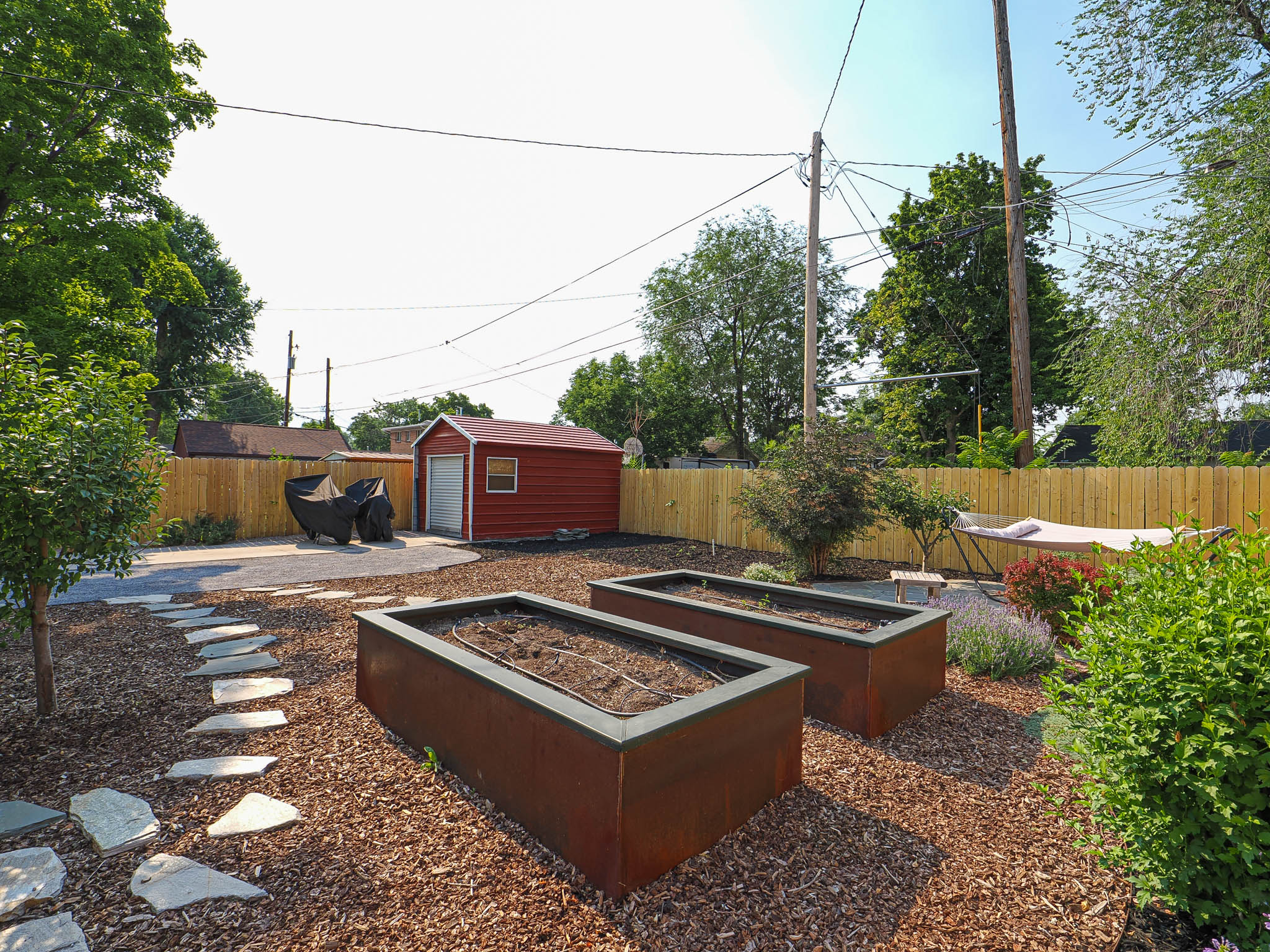 Expansive backyard featuring two raised garden beds, a flagstone path, and a wood chip ground cover