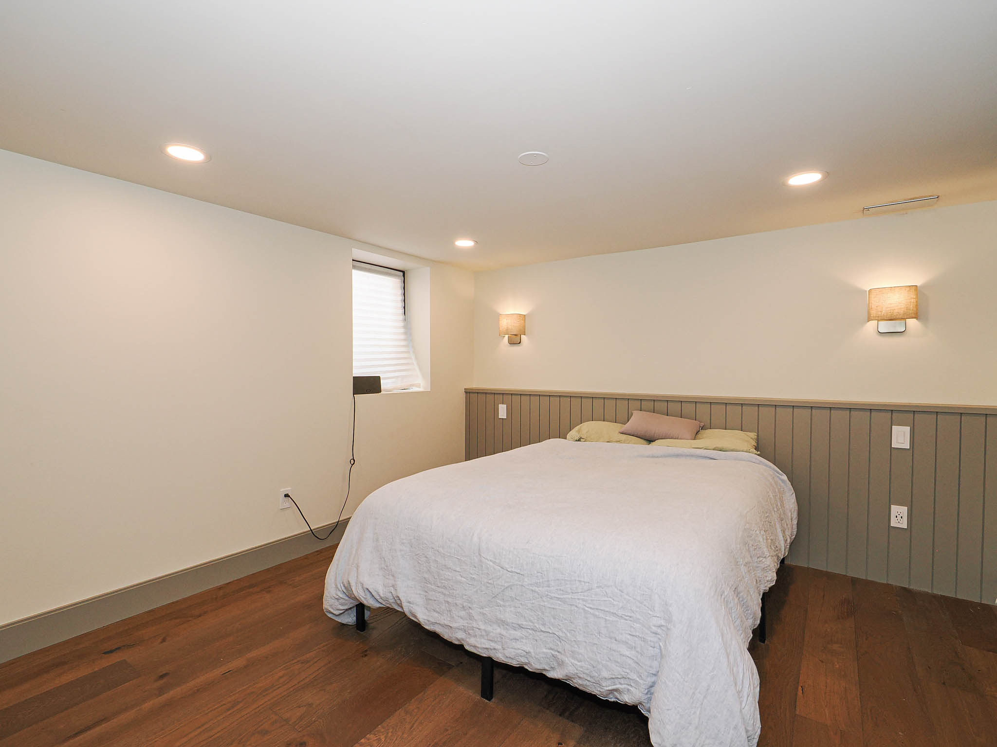 Bedroom featuring recessed ceiling lighting, wood-finish flooring, a baseboard trim, and wainscoting on the wall